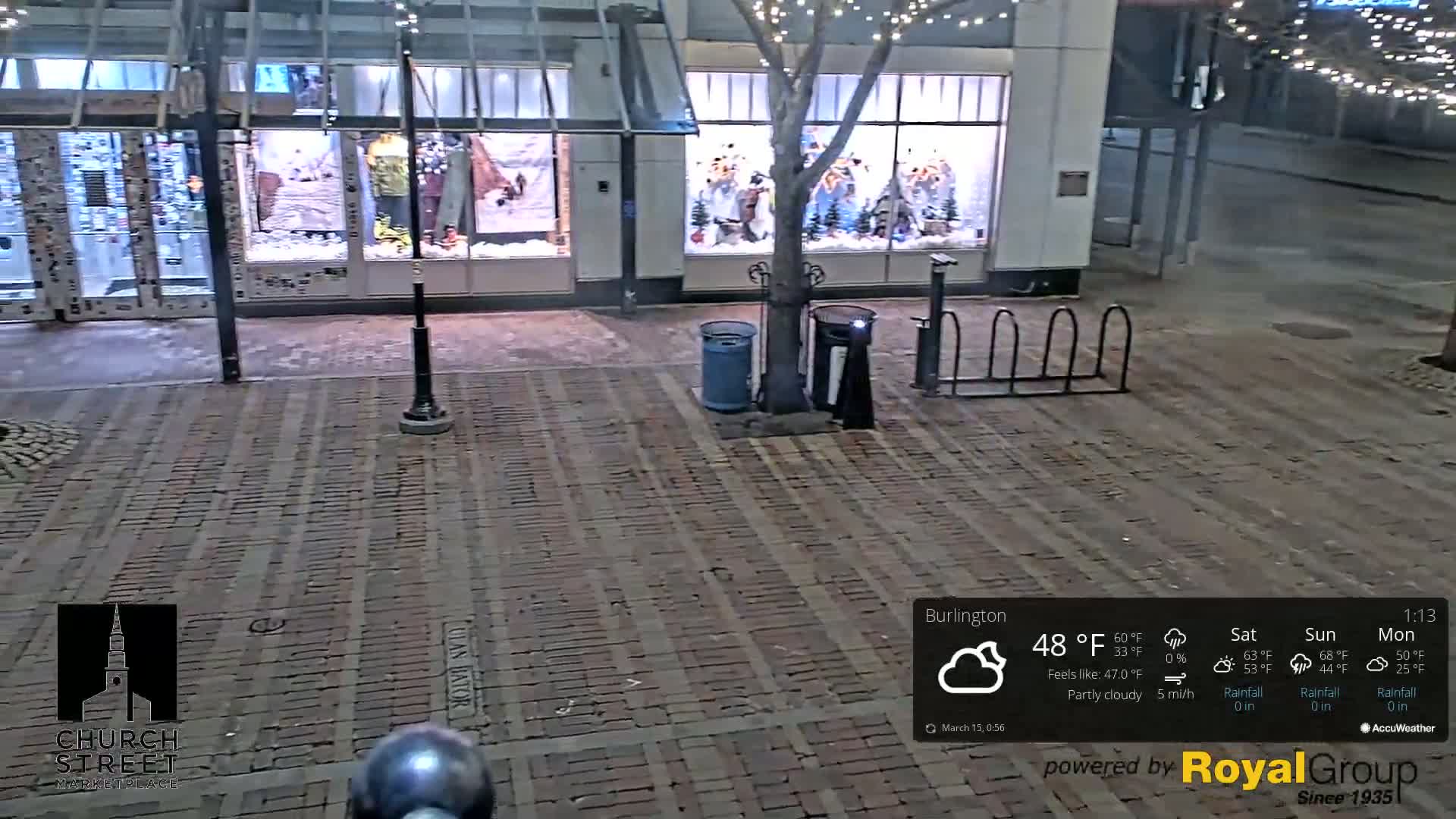 A brick-paved street at night, partly cloudy, with a storefront displaying winter clothing and a bike rack nearby.