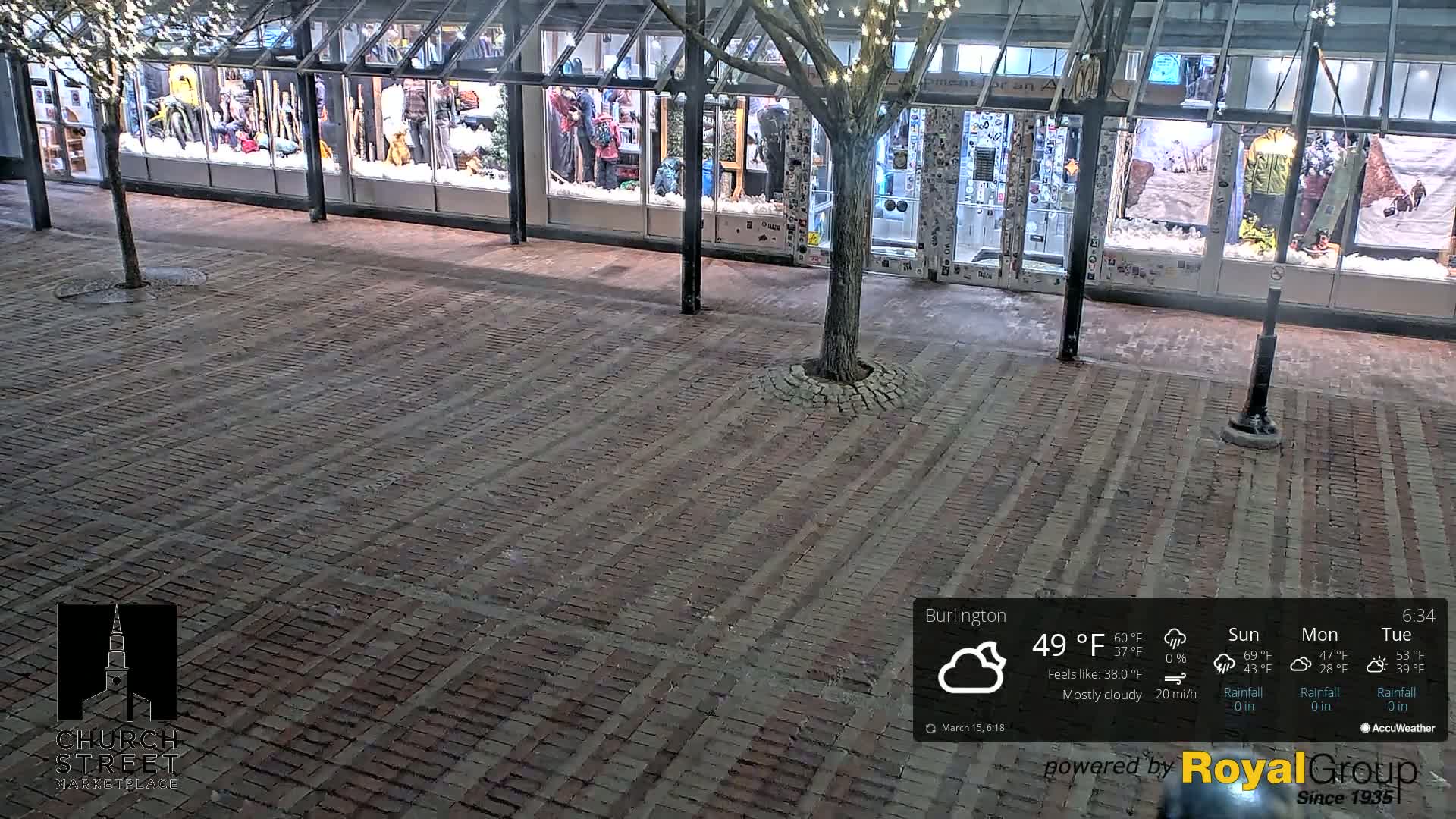 A brick paved area in front of a store with snow-covered window displays at night under mostly cloudy skies.