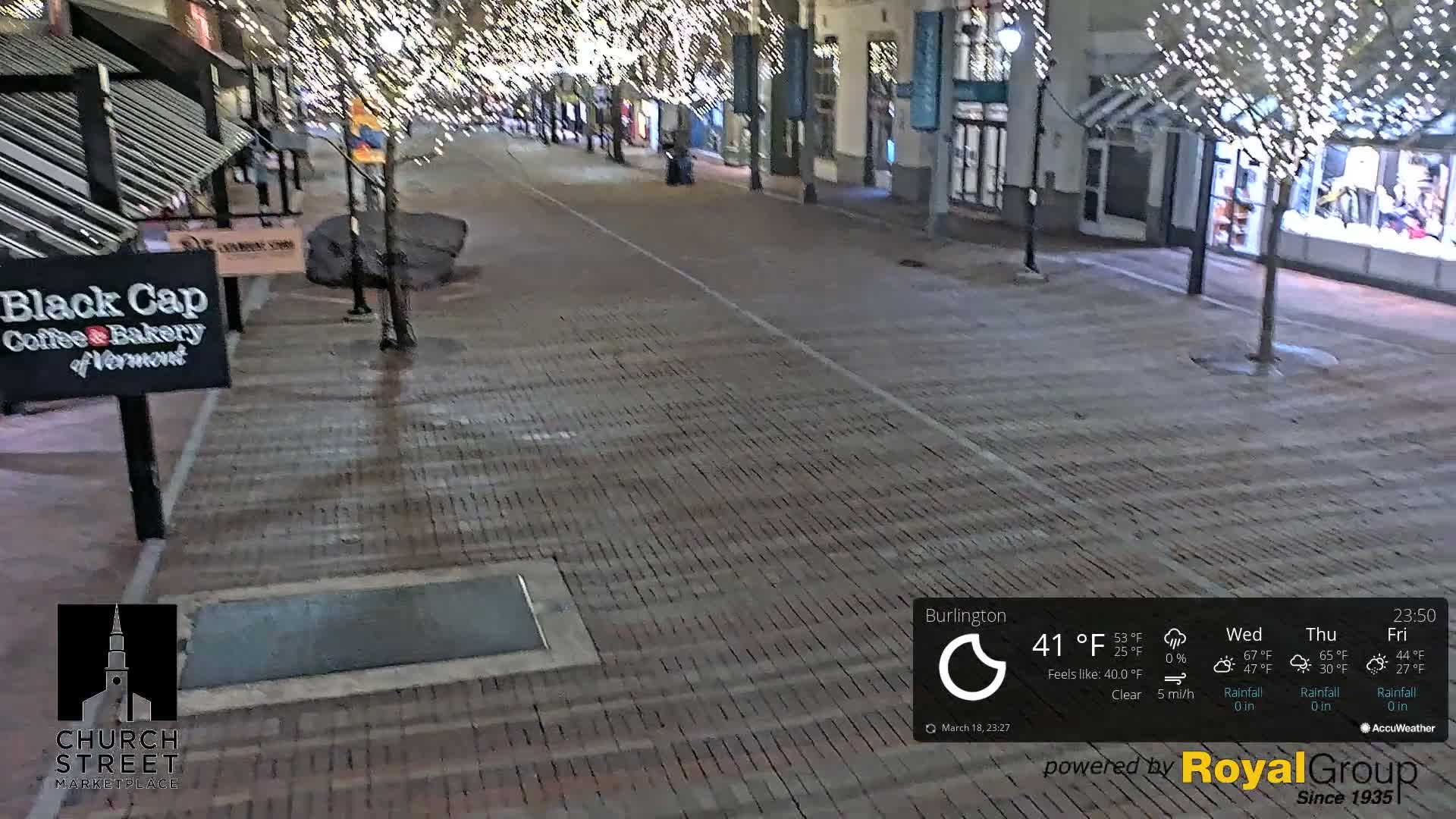 A brick-paved street at night, illuminated by string lights, is nearly deserted under clear skies with a temperature of 41°F and a light 5 mph wind.