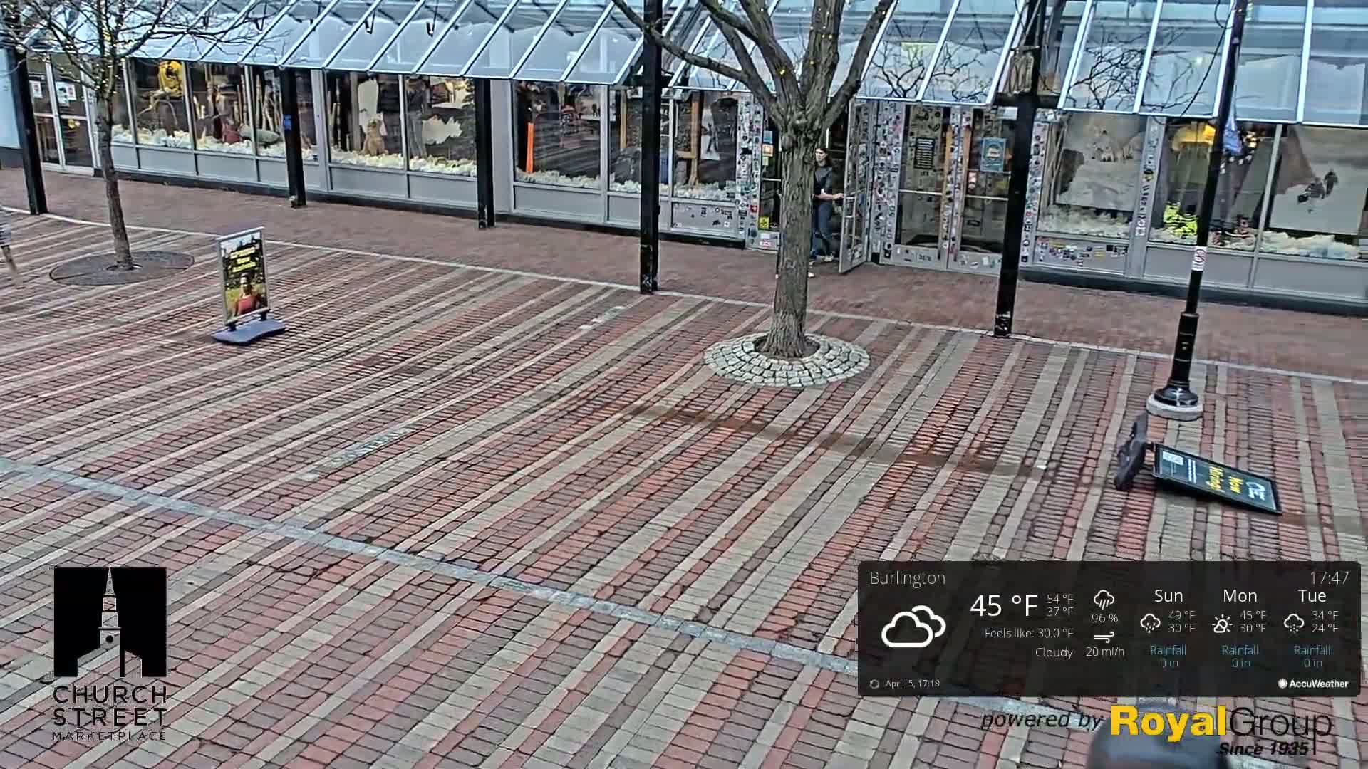 A brick plaza in front of a glass-fronted storefront under cloudy skies.