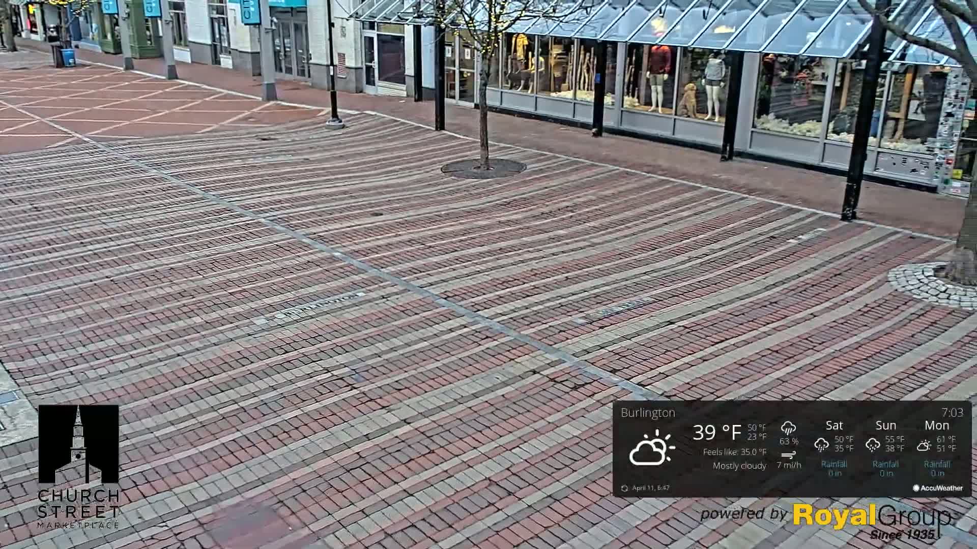 A mostly cloudy day reveals a brick-paved city street lined with storefronts.
