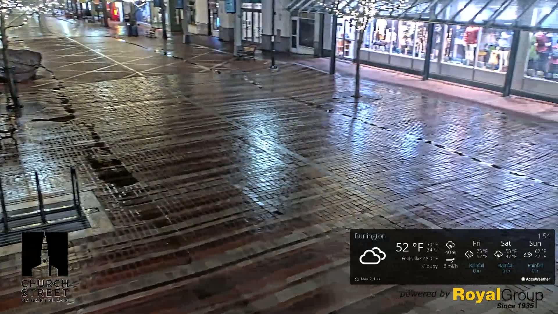 A wet, brick-paved street is shown at night under cloudy skies.