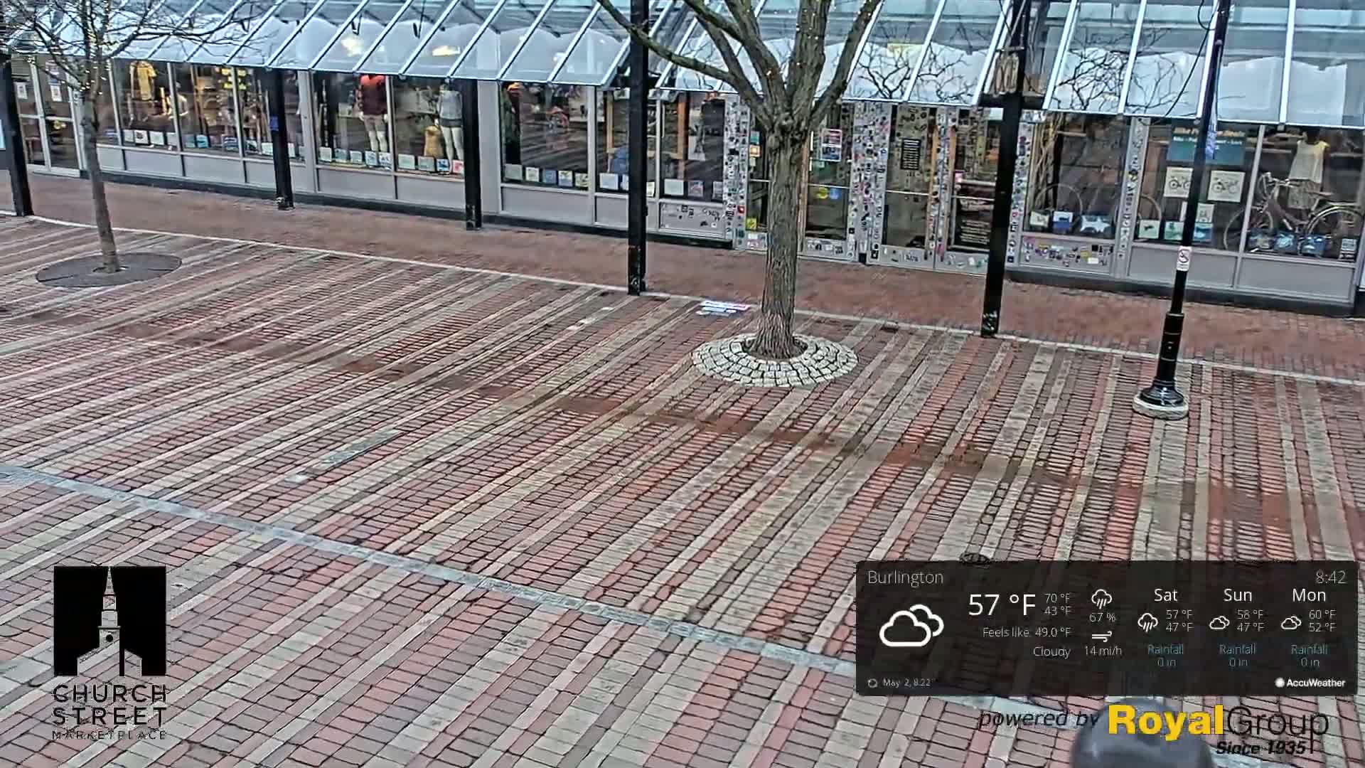 A brick-paved plaza sits in front of a glass-fronted building under a cloudy sky.