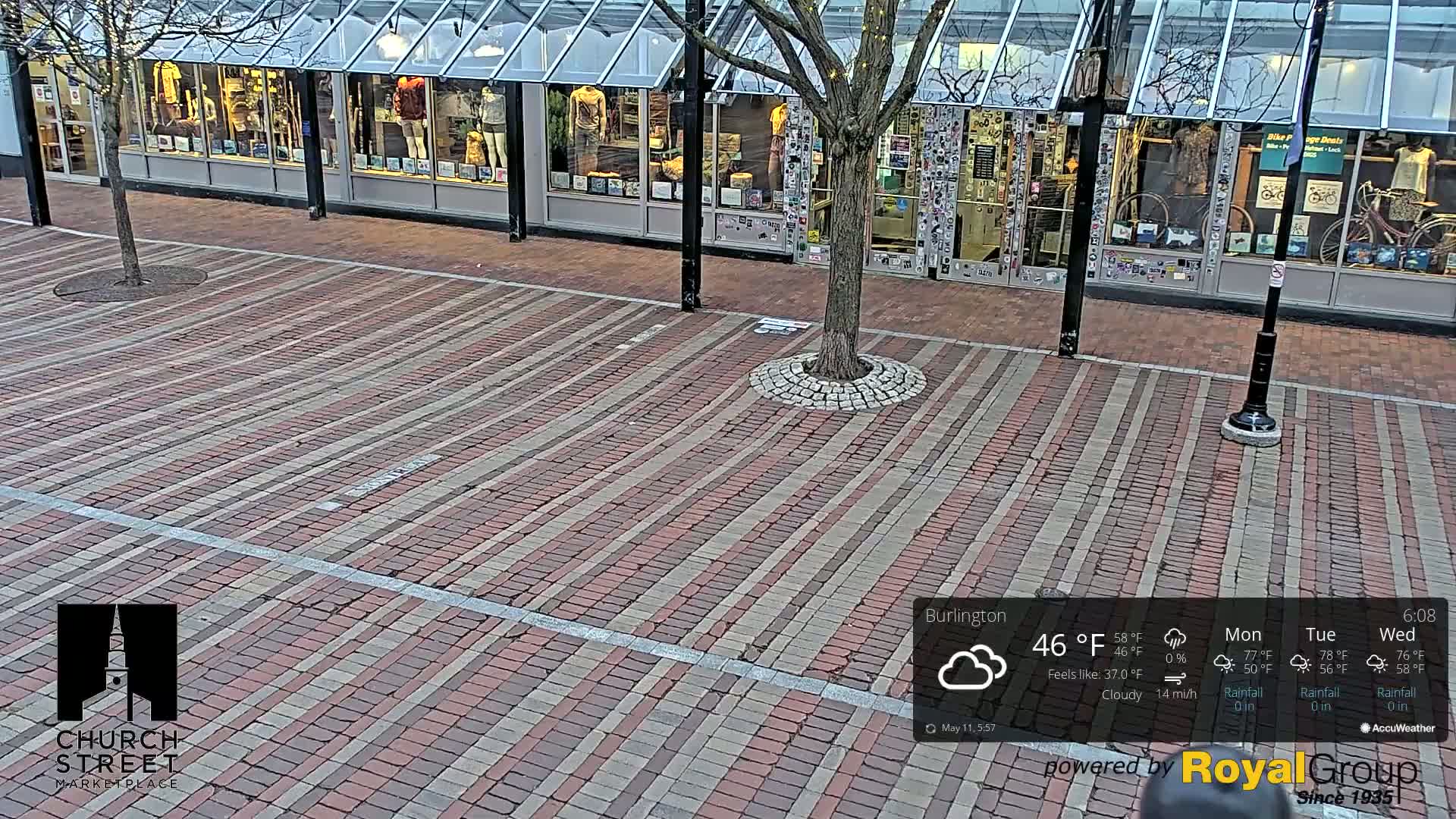 A brick paved area in front of several shops with glass fronts, under a cloudy sky.