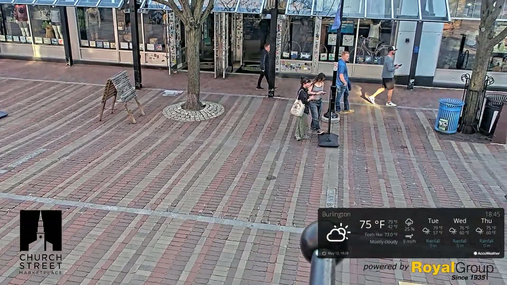 A brick-paved marketplace with several people walking around under mostly cloudy skies.