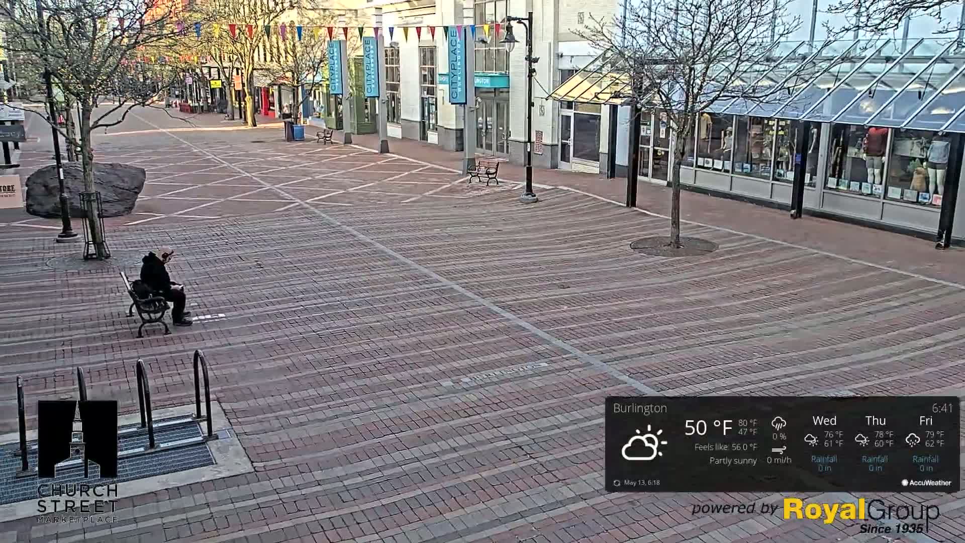 A person sits on a bench in a brick paved city square under partly sunny skies.