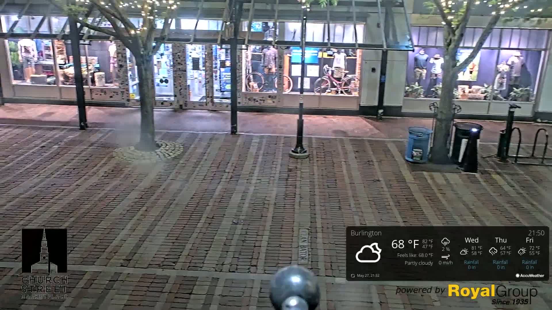 A nighttime view of a brick-paved street in front of a row of storefronts under a partly cloudy sky.