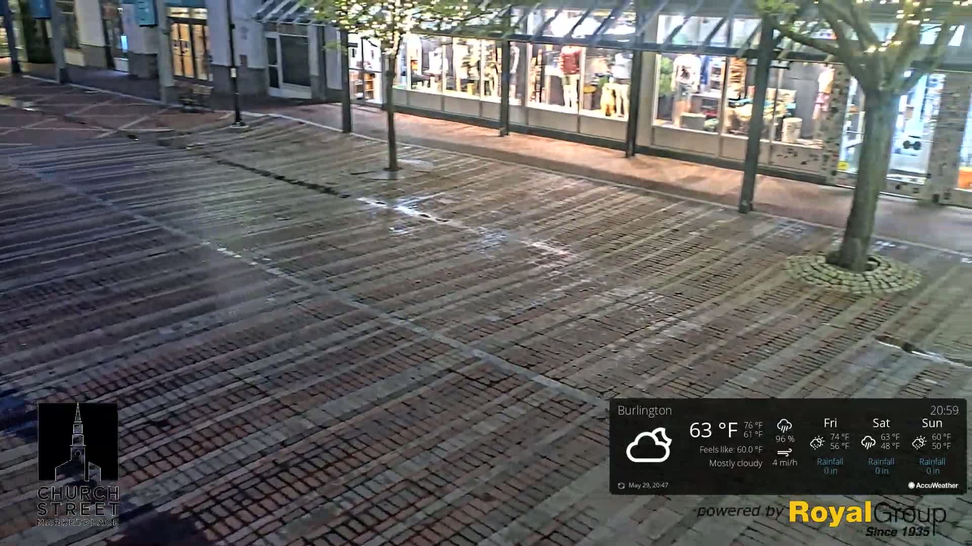 A mostly cloudy night scene shows a brick-paved street in front of a row of storefronts.