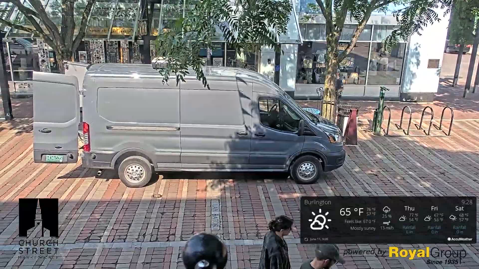 A gray van is parked on a brick street under mostly sunny skies.