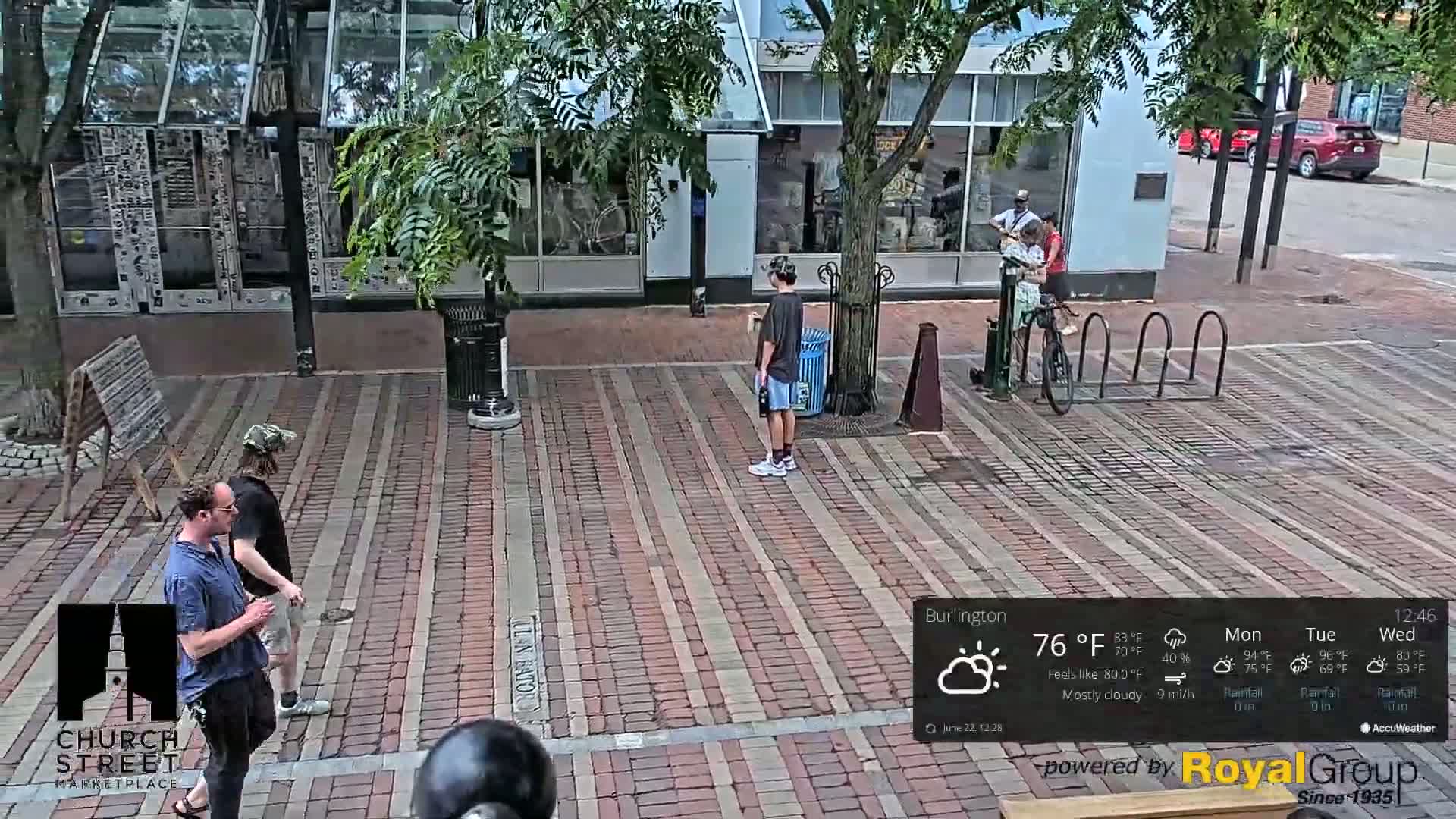 A brick paved street with several pedestrians, a bicycle rack with a bicycle, and a mostly cloudy sky.