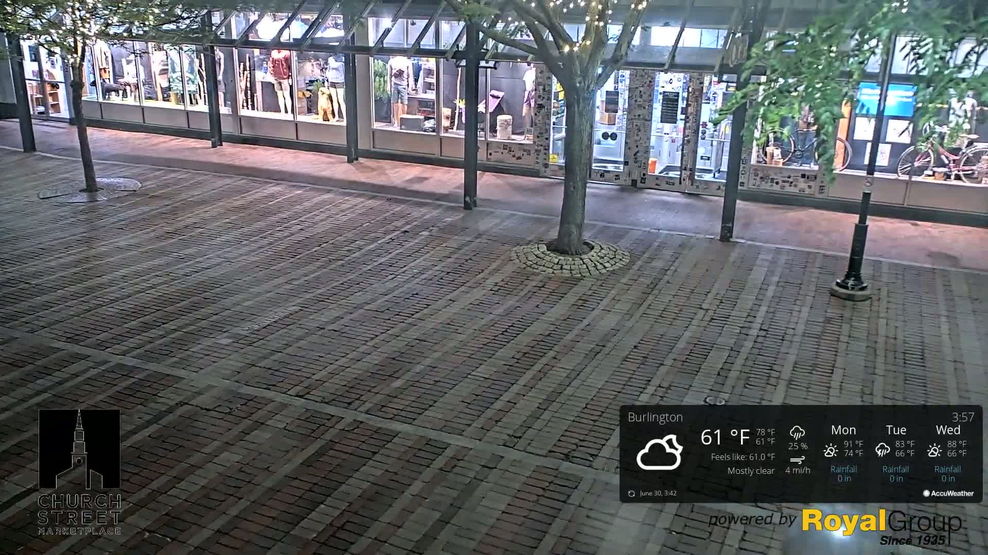 A brick paved area at night, mostly clear, with a tree and storefronts visible in the background.