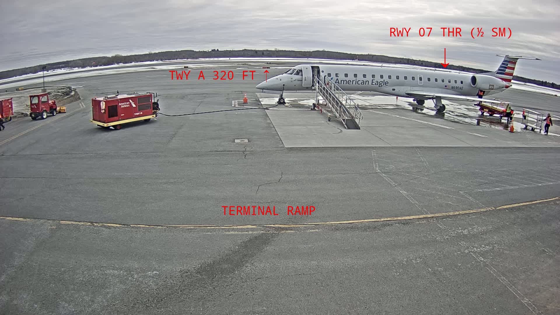 An American Eagle regional jet is parked at a terminal gate on an overcast day at an airport, with ground support equipment nearby.