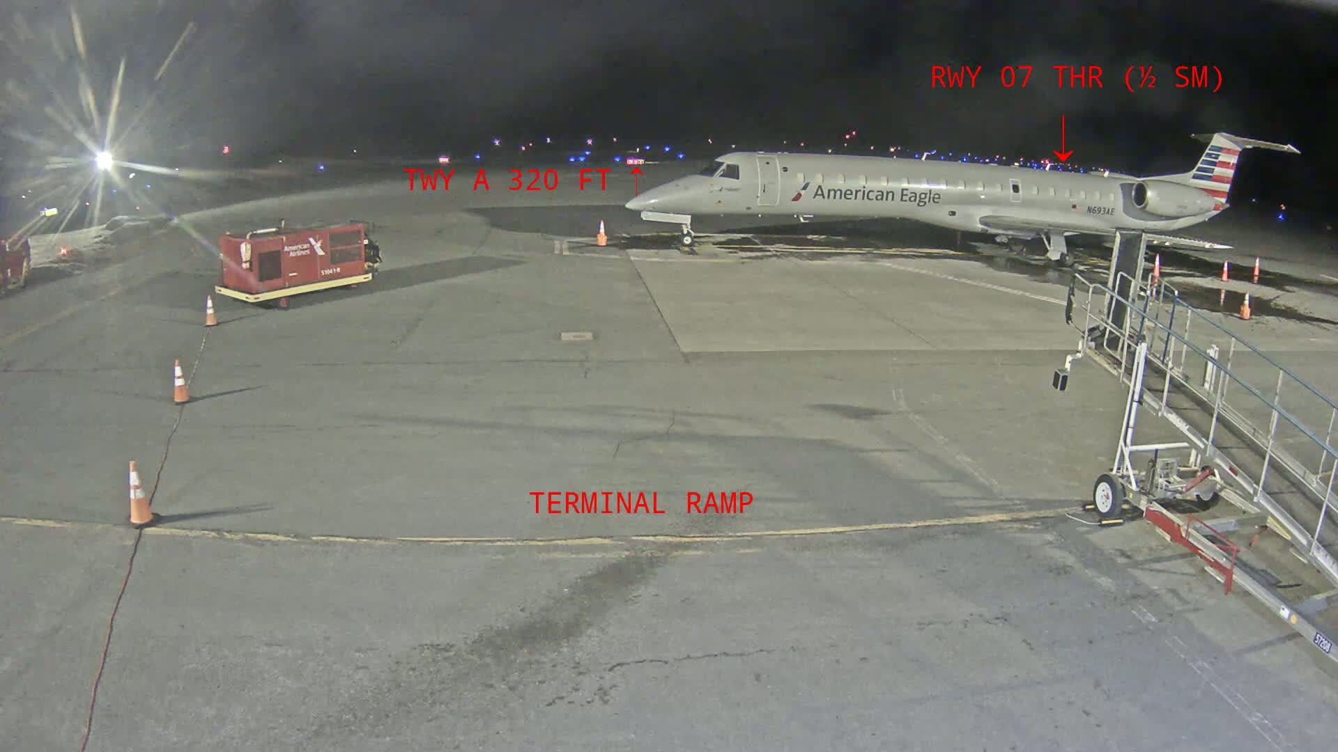An American Eagle regional jet is parked at night on a terminal ramp at an airport.