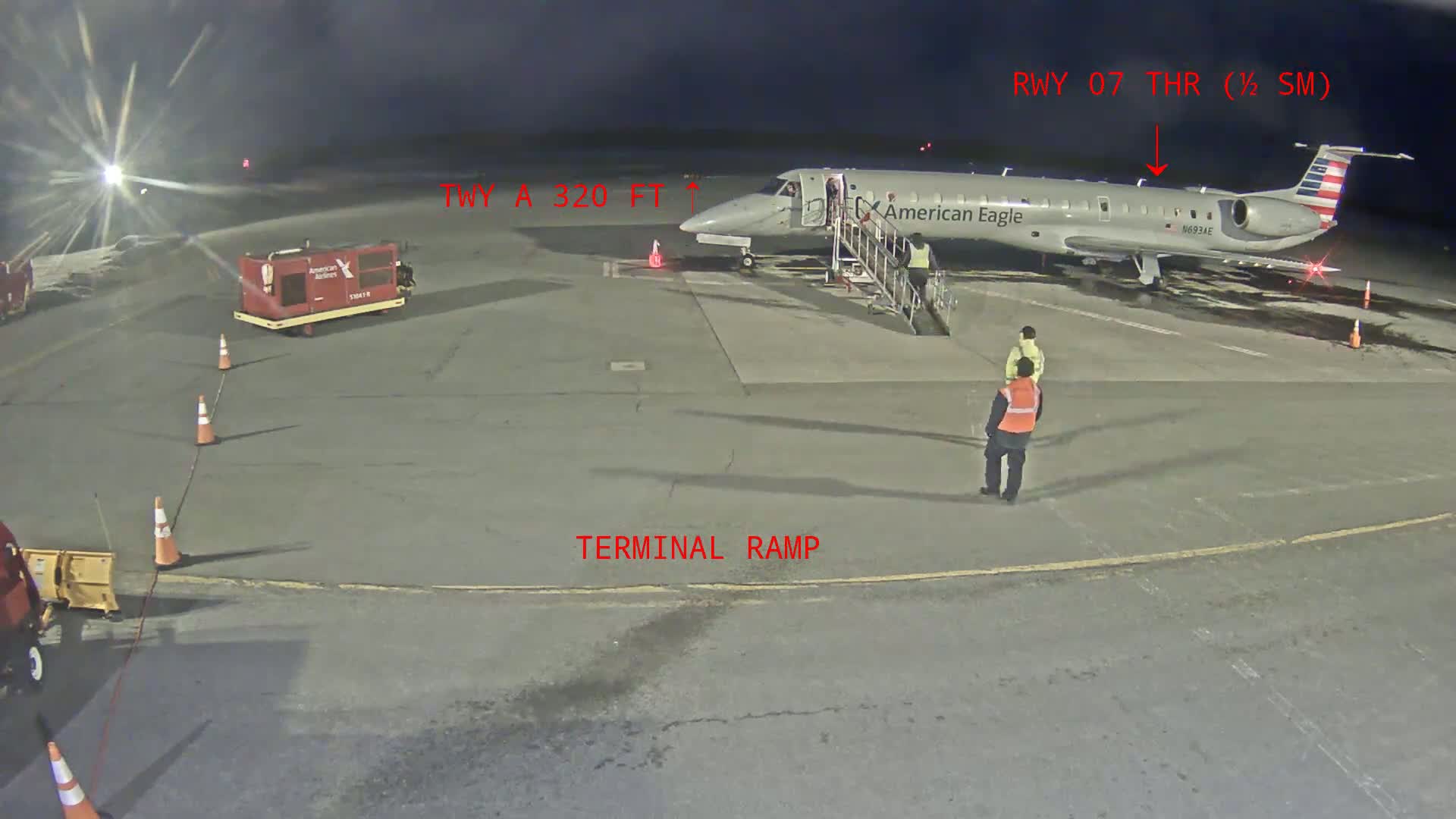At night, an American Eagle plane is parked at a terminal ramp with several ground crew members nearby.