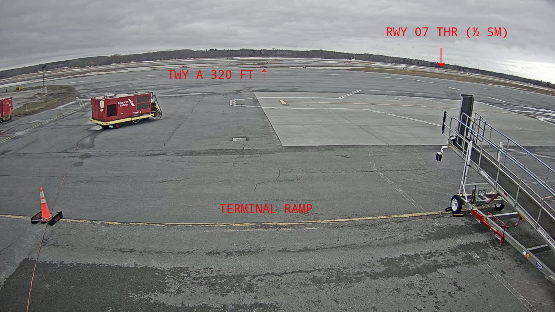 An overcast day at an airport shows a terminal ramp, a small ground support vehicle, and a jet bridge; in the distance, a runway is visible.