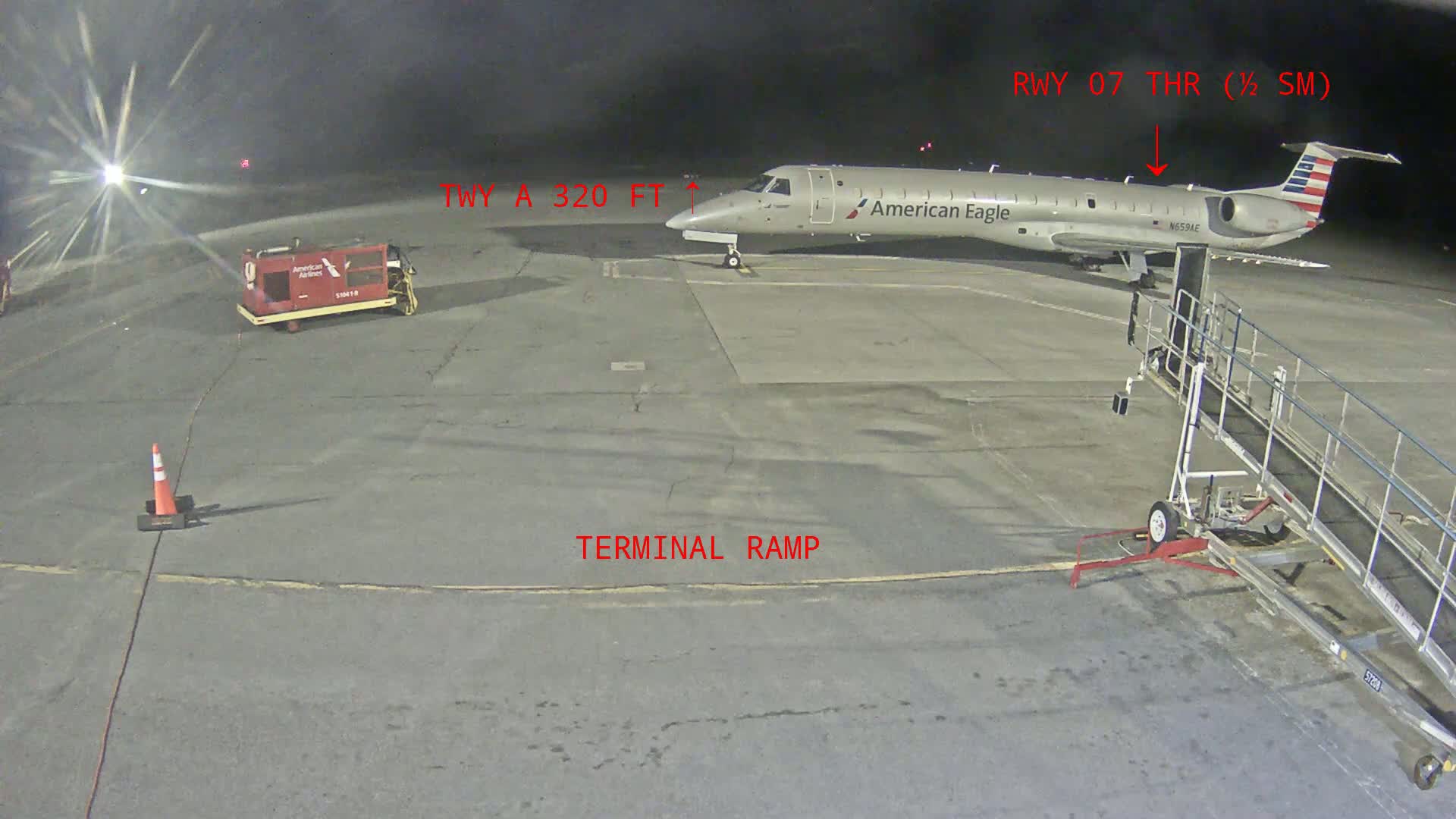 At night, an American Eagle regional jet is parked on a terminal ramp near a jet bridge.