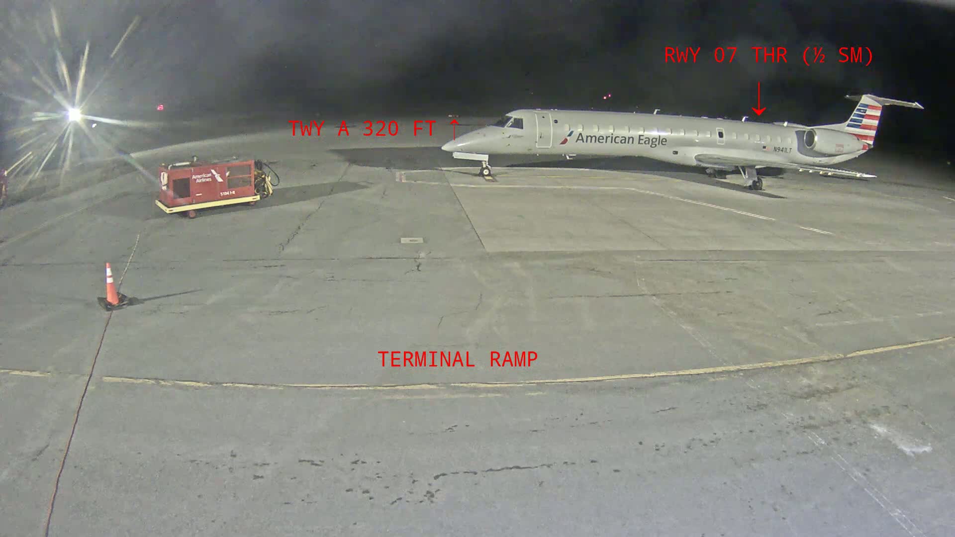 At night, a gray American Eagle airplane is parked on a tarmac next to a baggage tug.