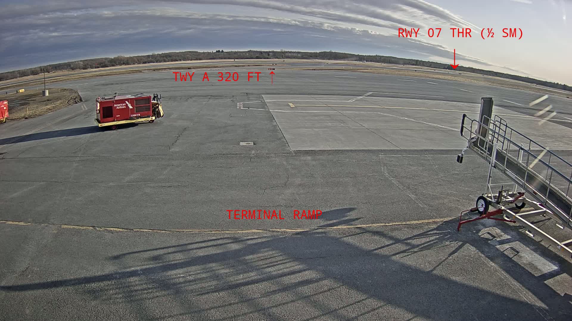 An airport tarmac under a partly cloudy sky shows a ground service vehicle, a jet bridge, and a runway extending to the horizon.