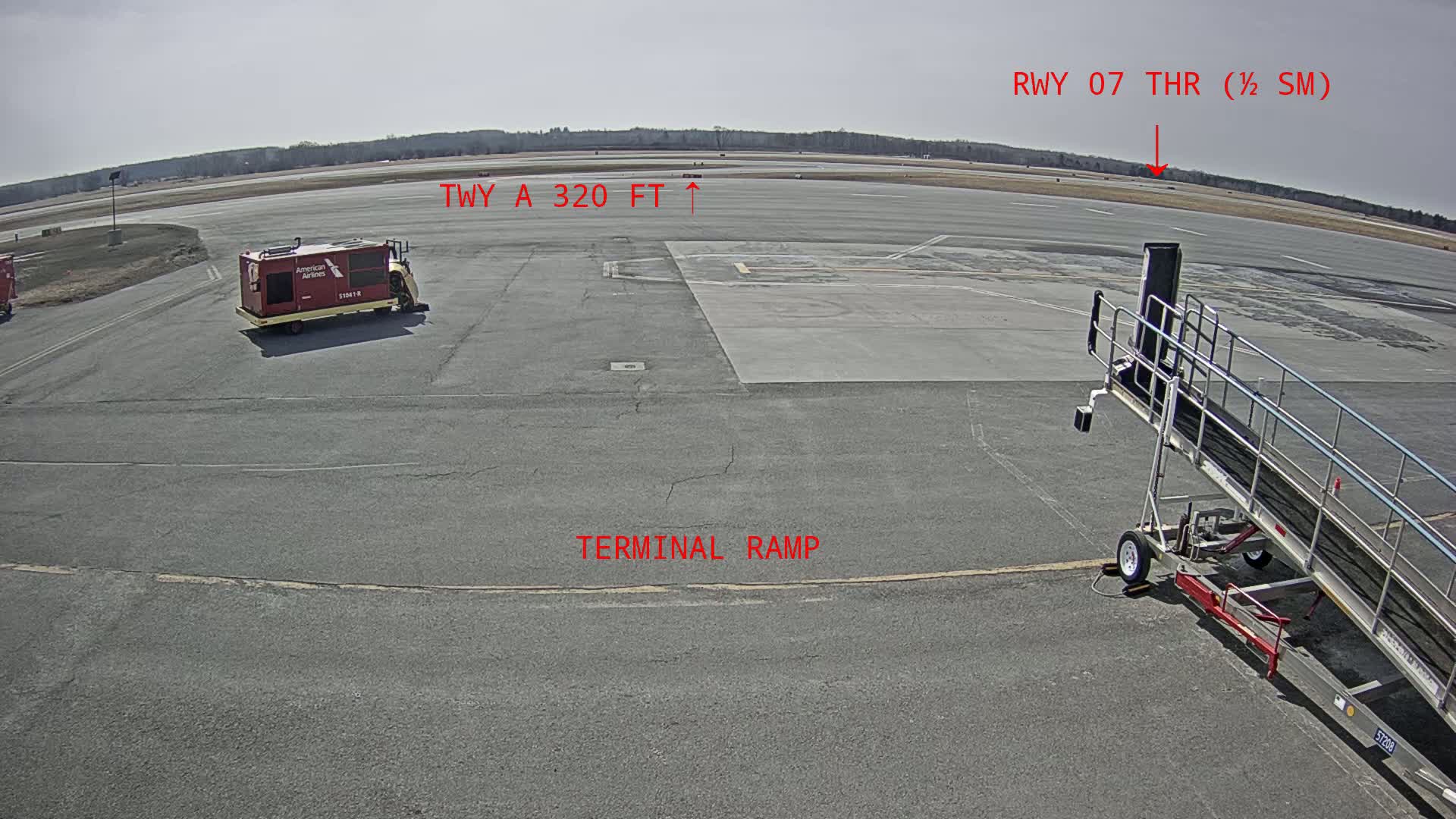 A tarmac view shows an airport terminal ramp with a jet bridge, a baggage cart, and a runway in the distance under a clear, sunny sky.