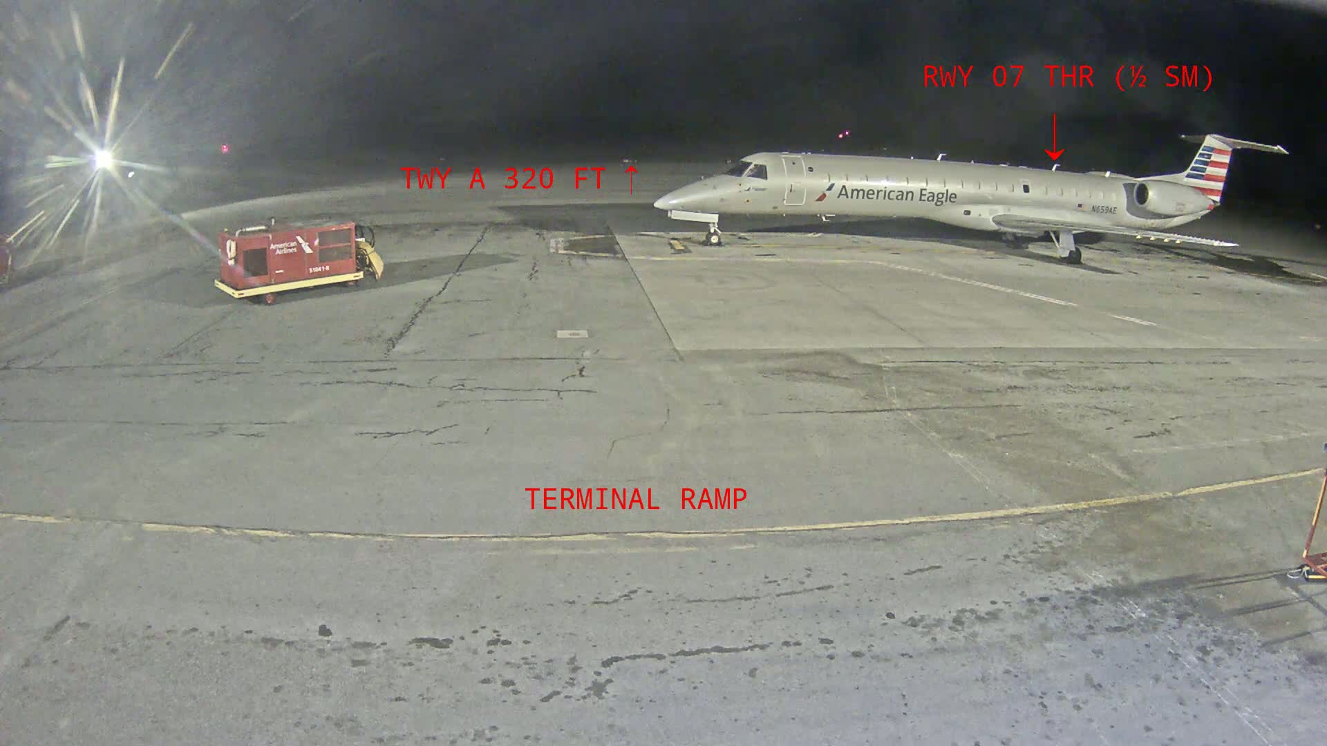 At night, an American Eagle regional jet is parked on a tarmac next to a baggage tug.