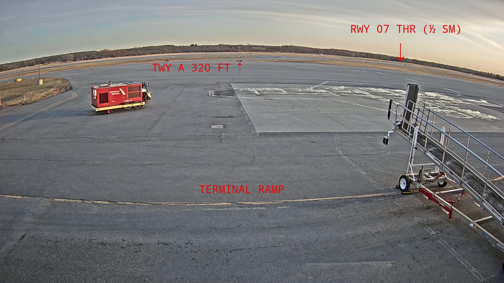 A tarmac view shows a small red ground service vehicle, a jet bridge, and a runway under a partly cloudy sky.