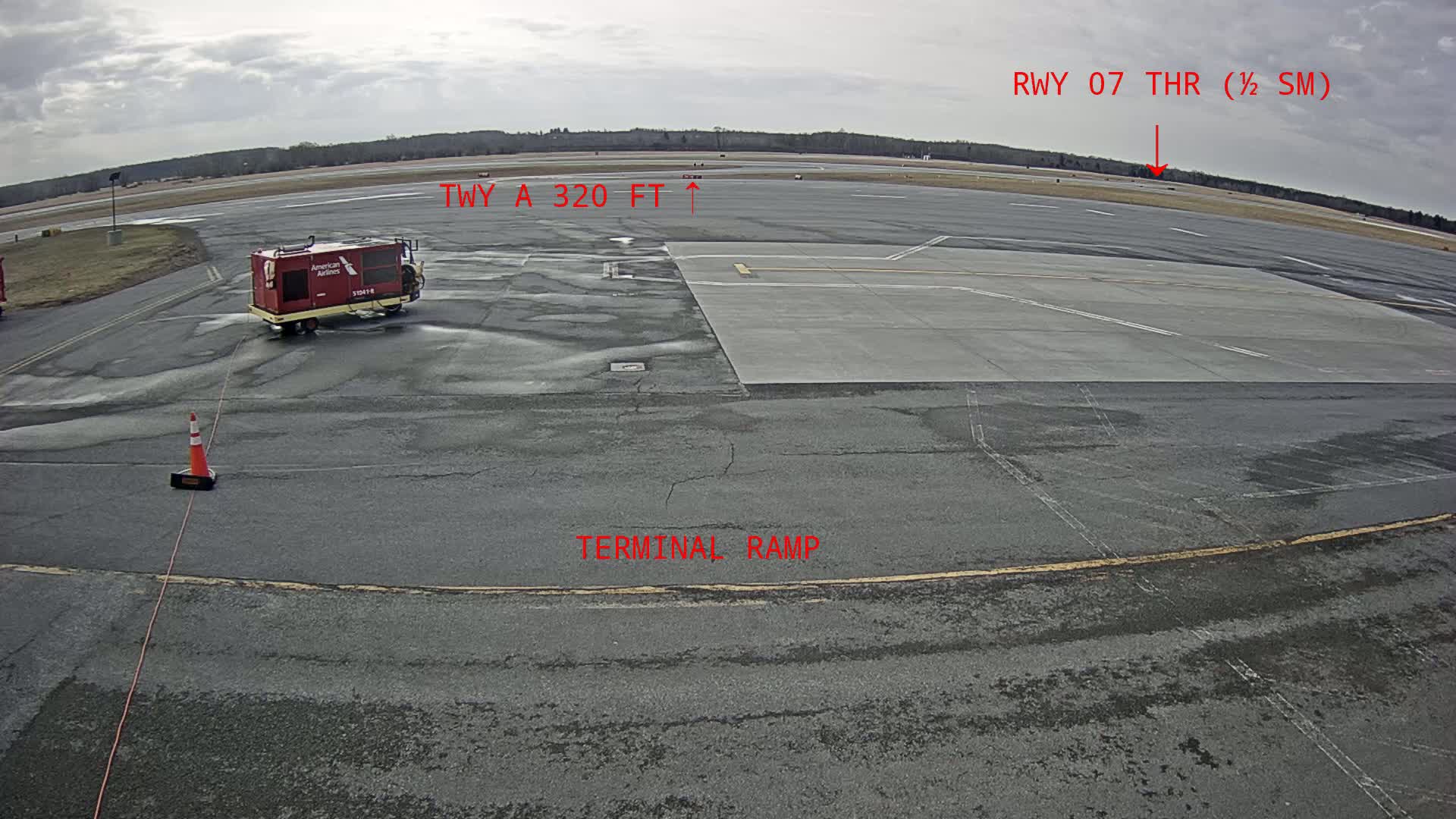 A tarmac at an airport under an overcast sky shows a small service vehicle and a runway in the distance.