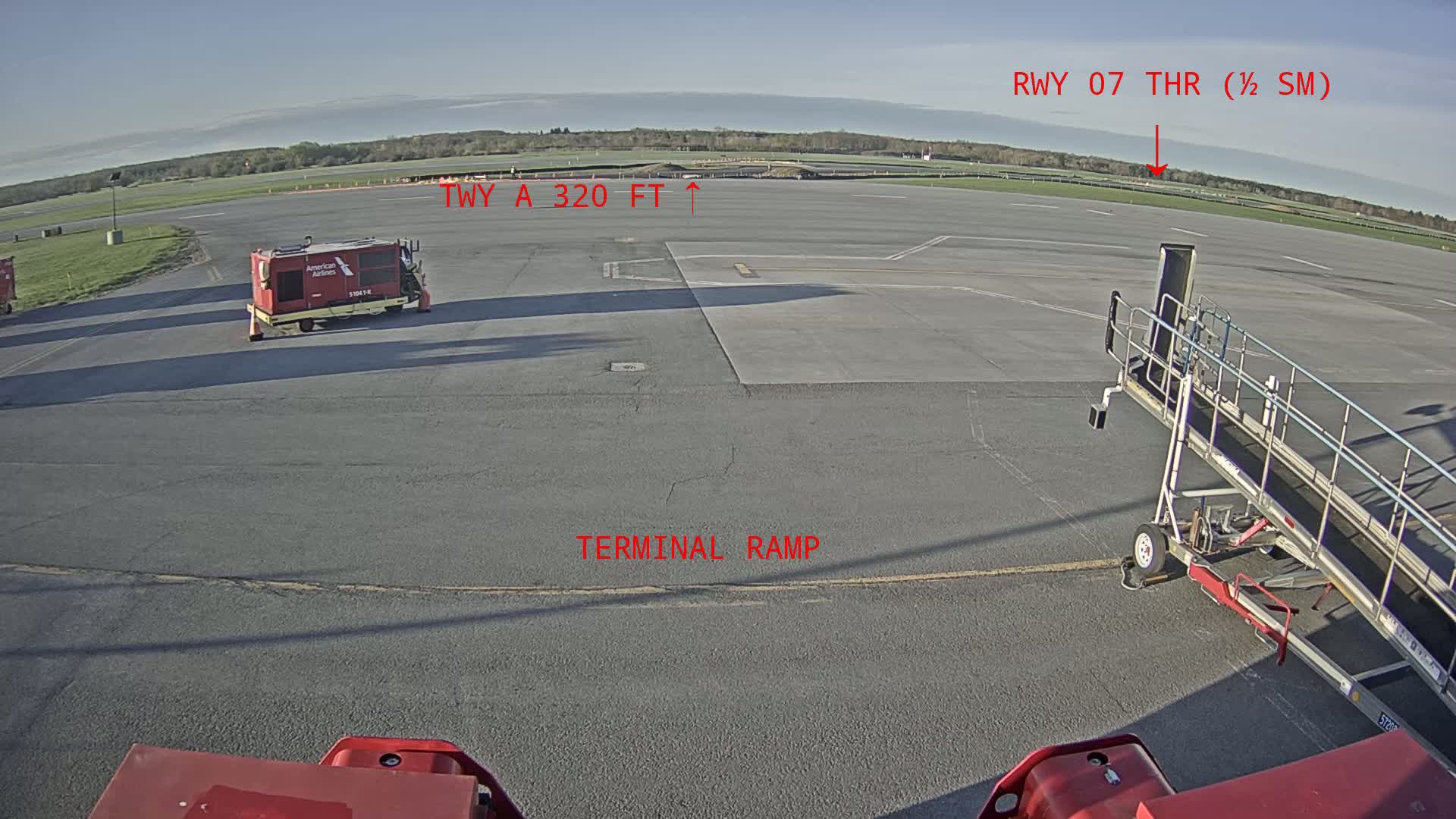 A tarmac view shows an airport terminal ramp with a jet bridge and ground support equipment under a clear, sunny sky.