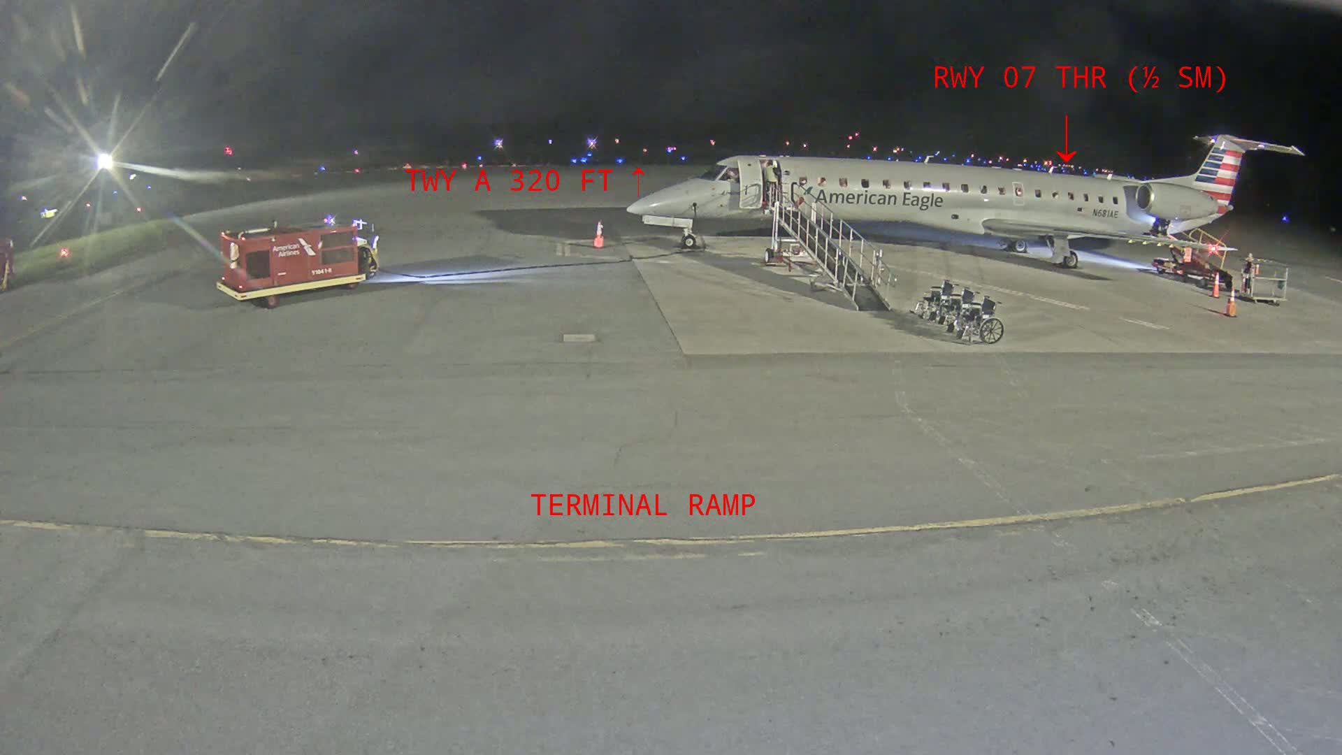 A regional jet is parked at a terminal gate at night on a tarmac, with baggage carts and ground support equipment nearby.