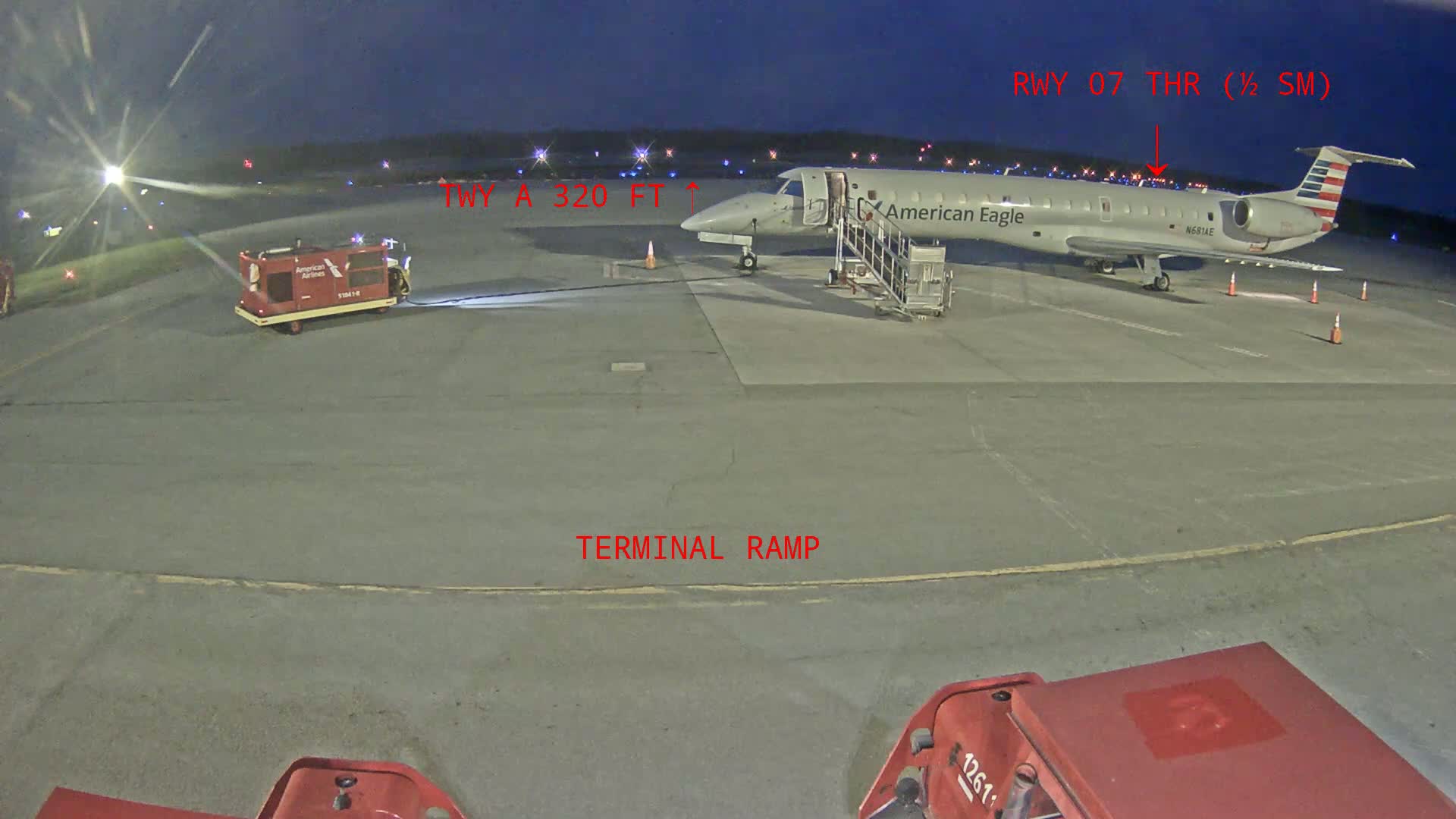 An American Eagle regional jet is parked at a terminal ramp at night, under partly cloudy skies.
