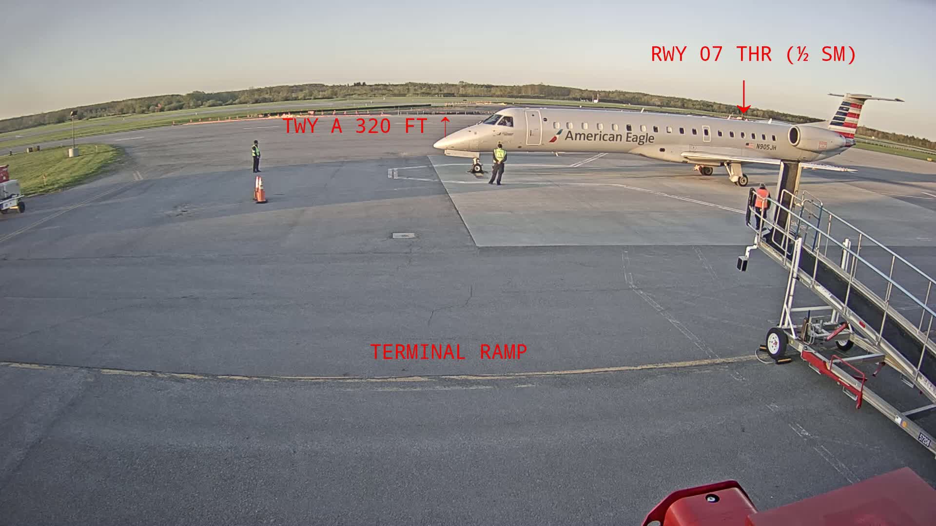 An American Eagle regional jet is parked at a terminal ramp on a clear day at an airport, with a jet bridge attached.