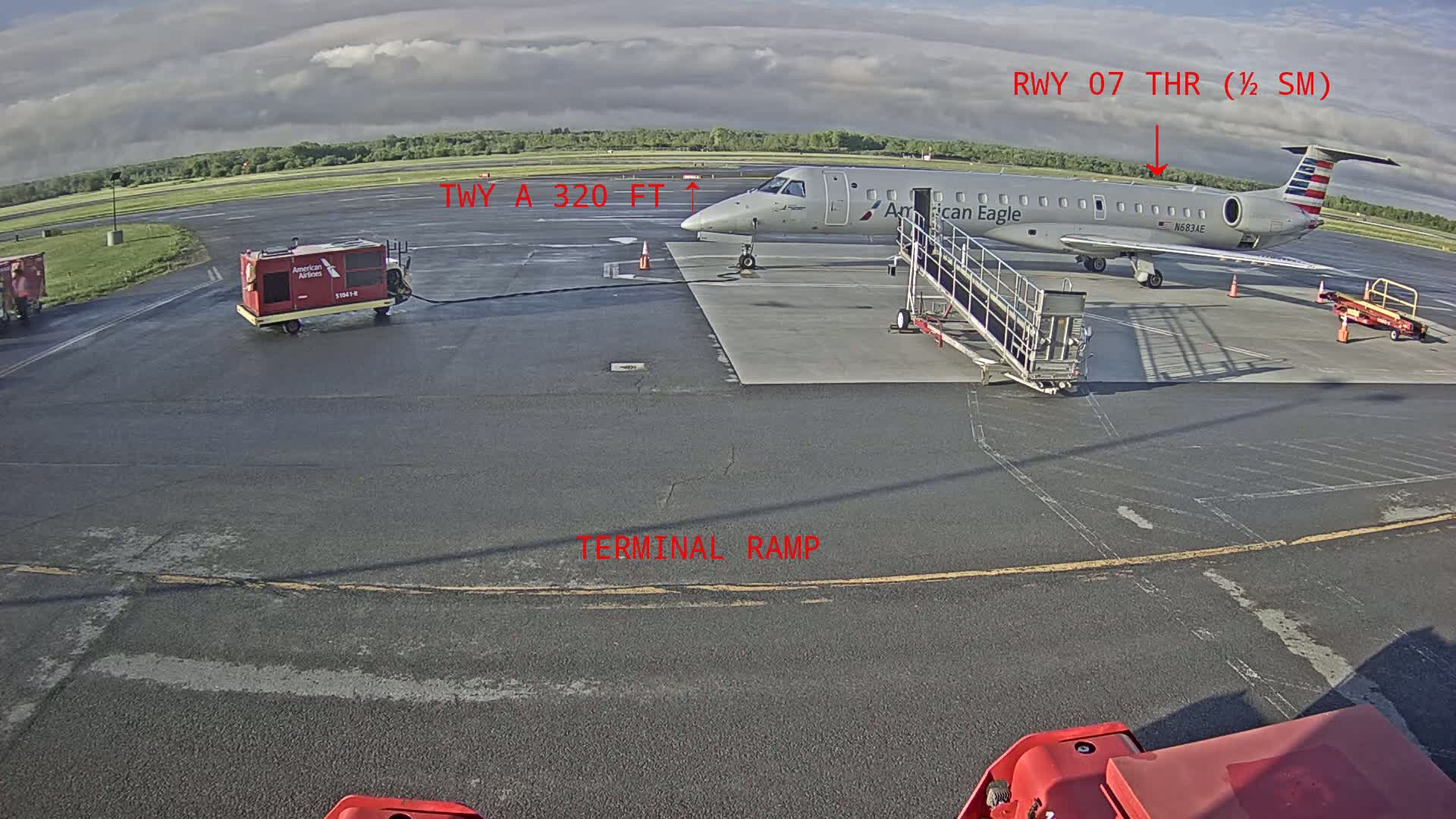 An American Eagle regional jet is parked at a terminal gate on a partly cloudy day.