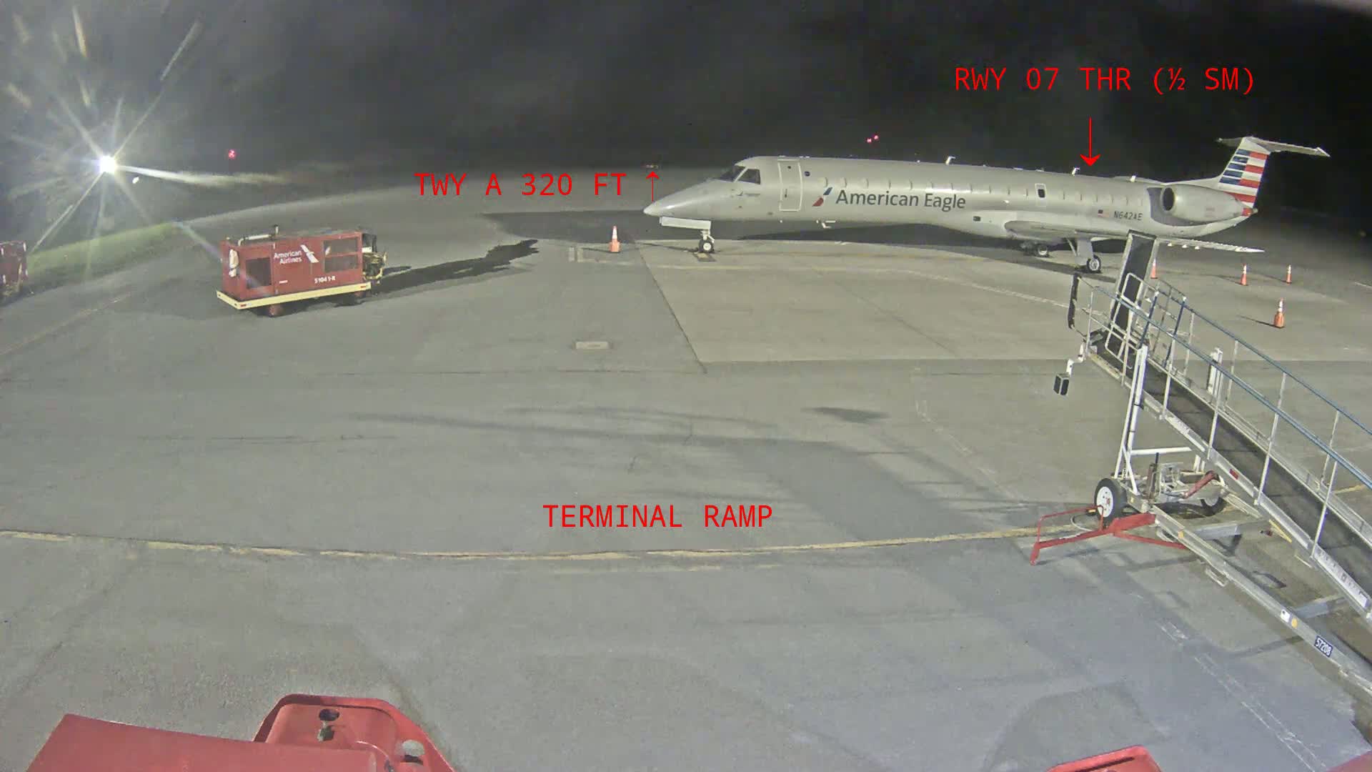 At night, an American Eagle regional jet is parked at a terminal ramp with ground support equipment nearby.