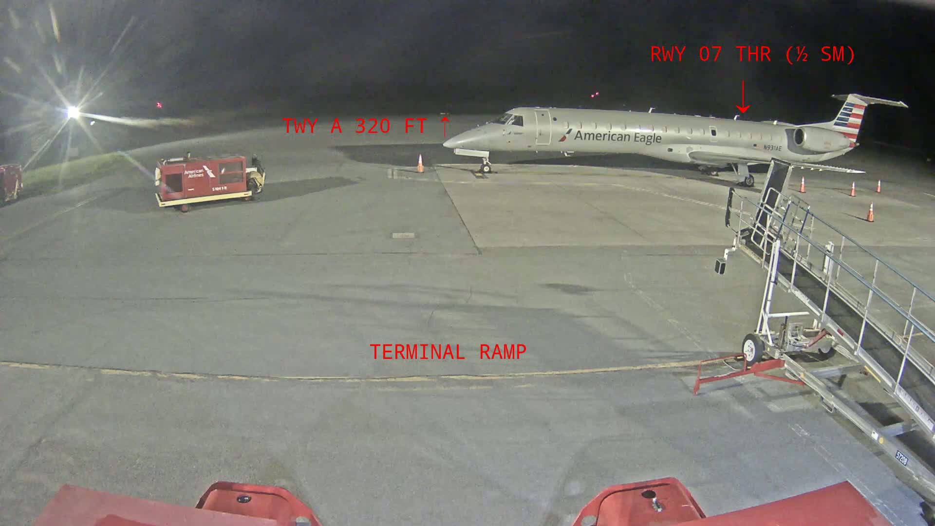 At night, an American Eagle regional jet is parked on a terminal ramp near a mobile staircase, with airport service vehicles nearby.