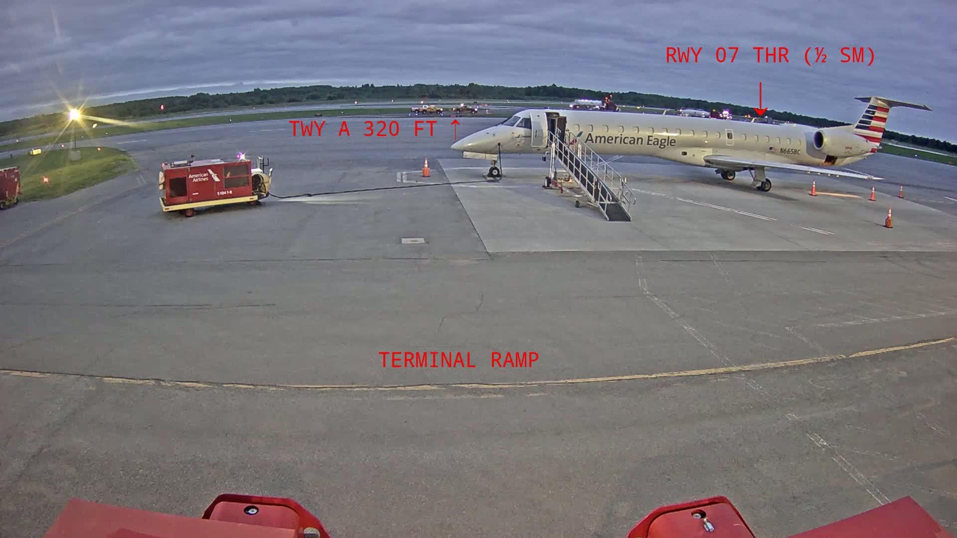 An American Eagle regional jet is parked at a terminal ramp on an overcast day.