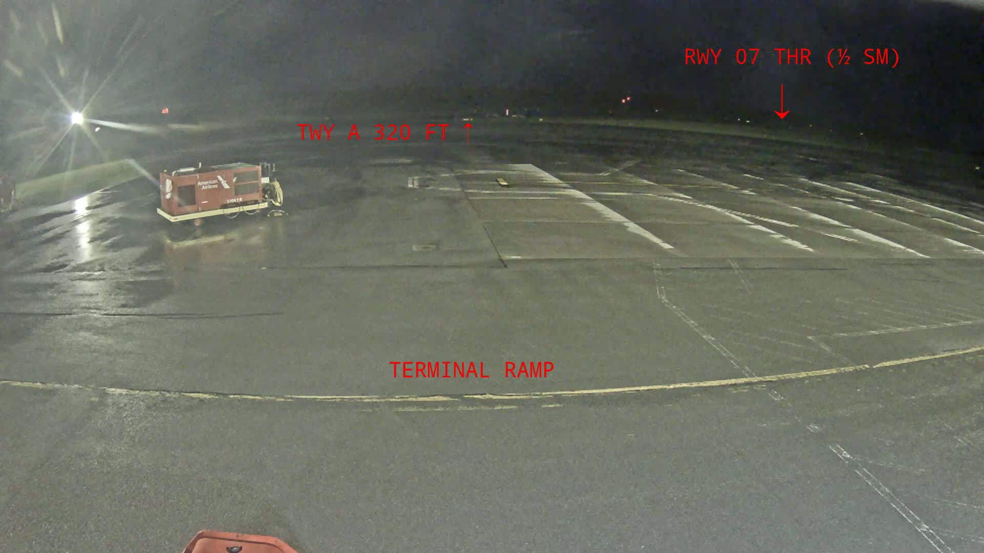 A wet, dark airport terminal ramp at night, with a ground support vehicle parked nearby.