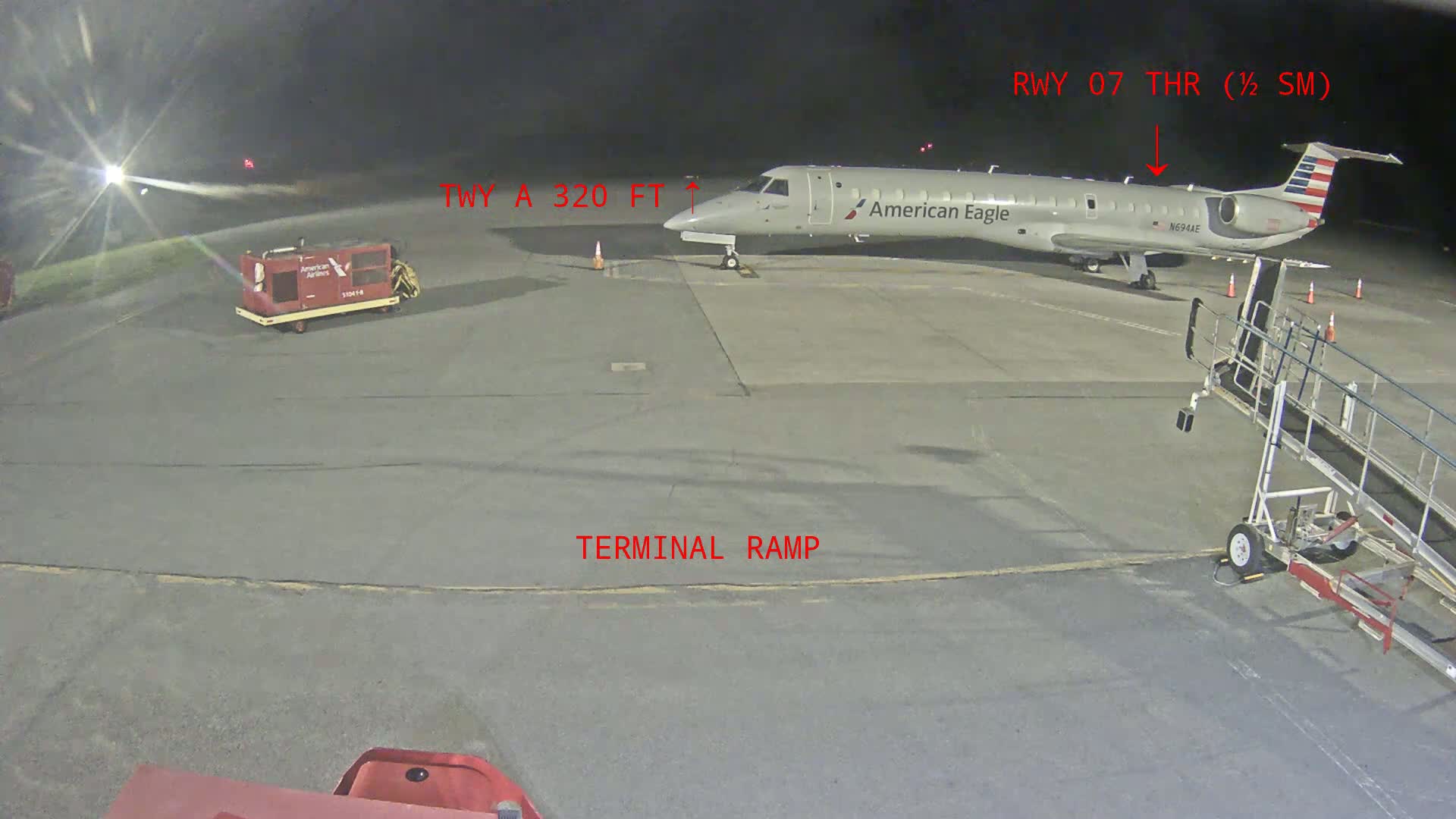At night, a passenger plane is parked at a terminal ramp, with a jet bridge connected to it.