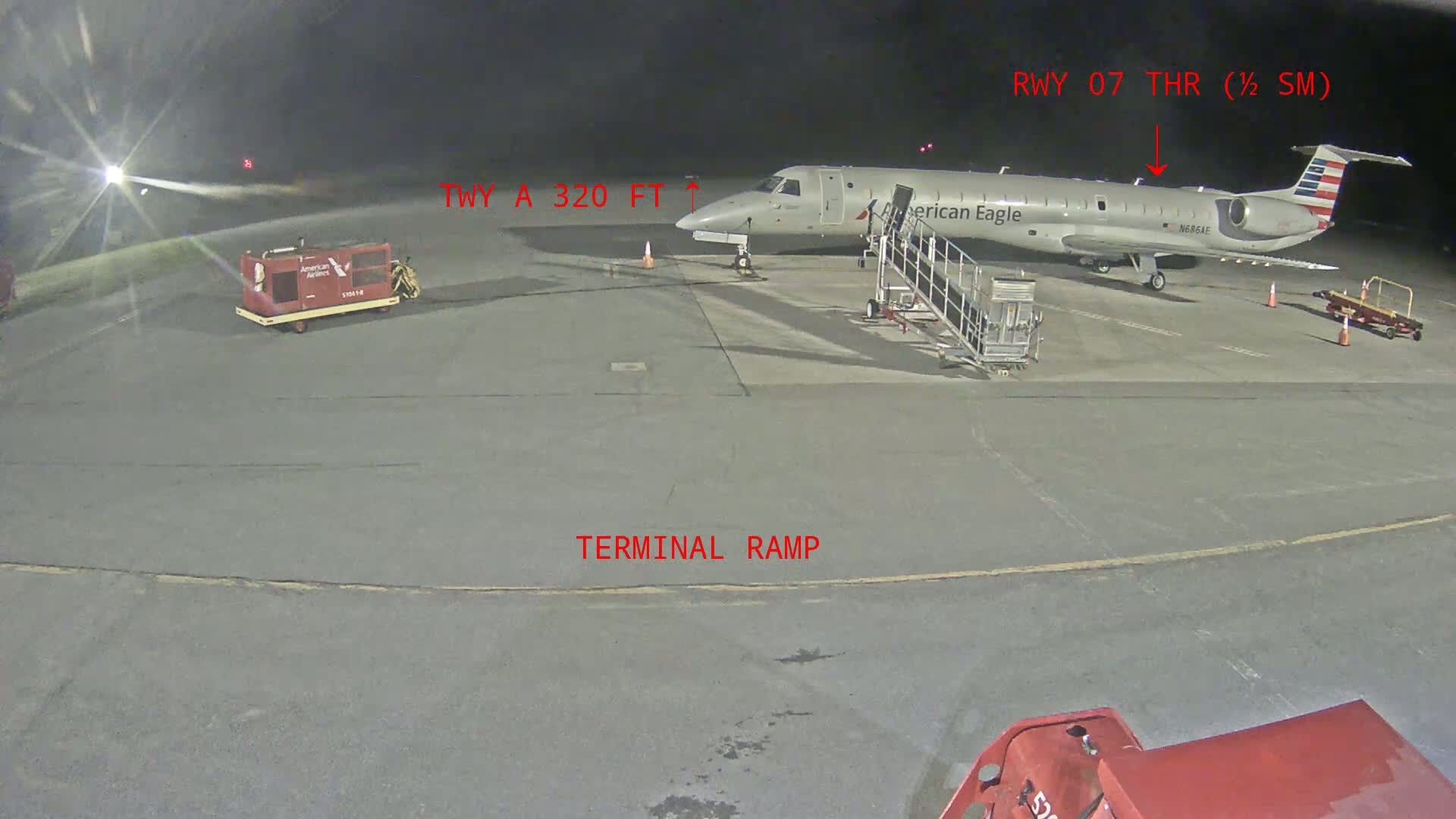 At night, an American Eagle airplane is parked at a terminal ramp with ground support equipment nearby.
