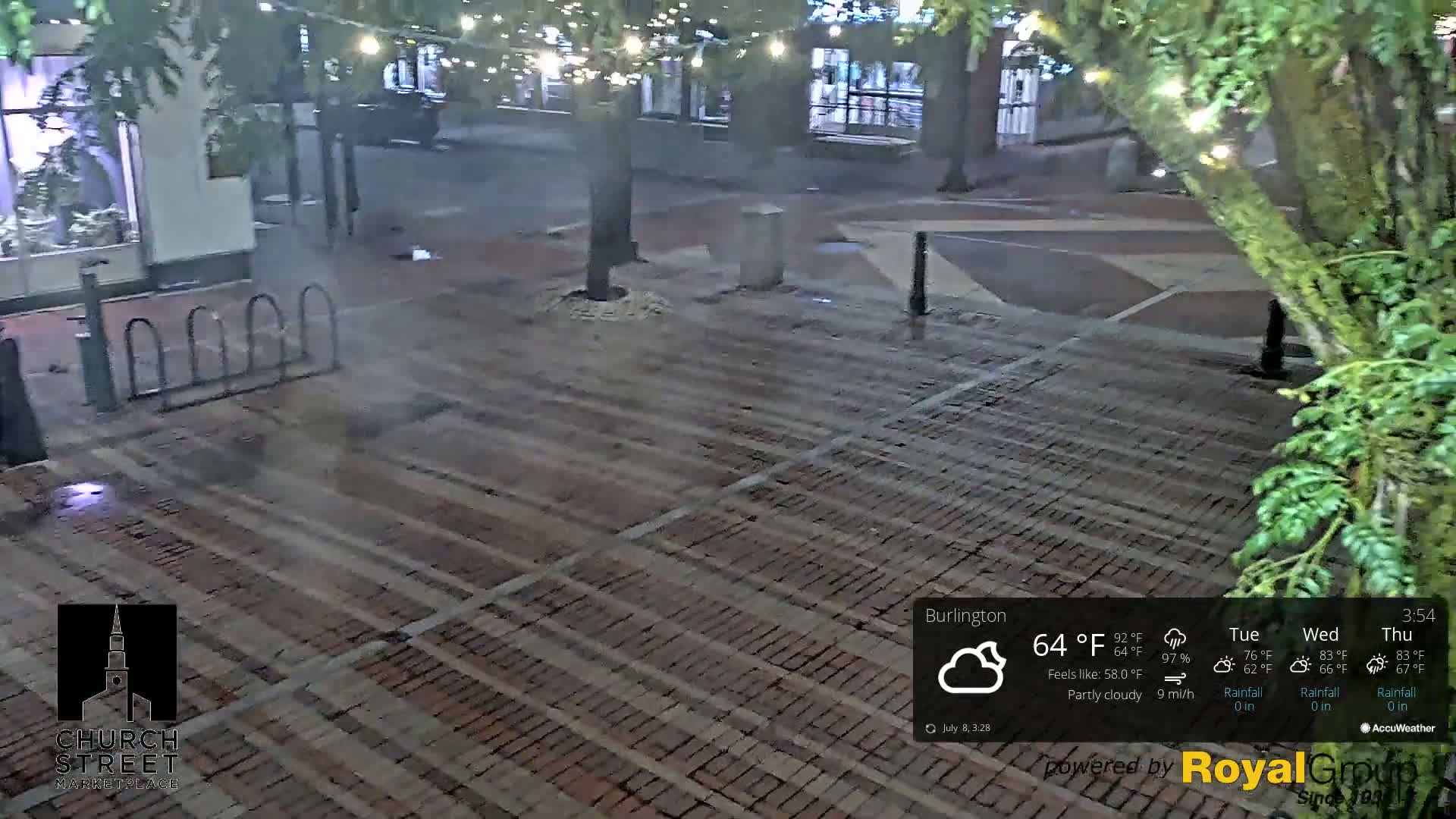 A brick paved area at night, partially lit with string lights, under partly cloudy skies.
