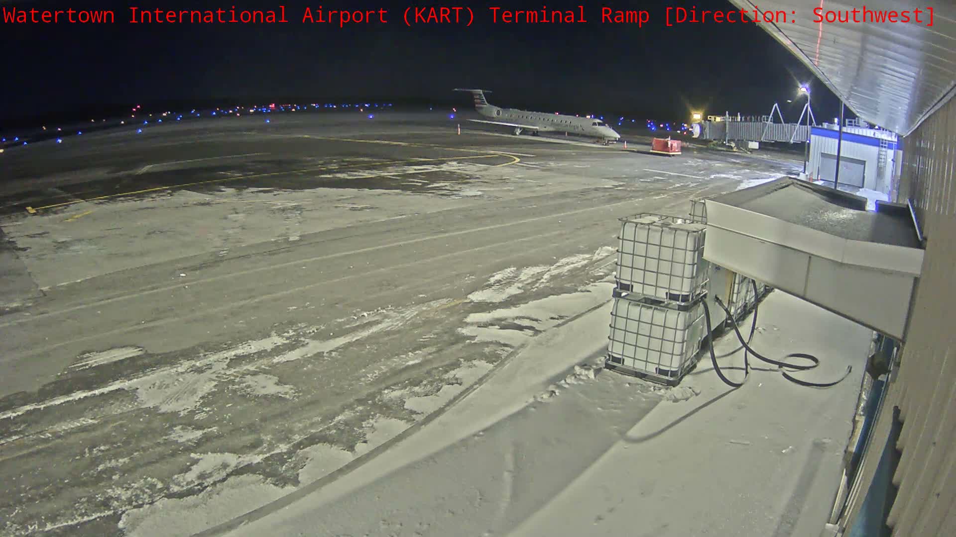 A regional jet is parked at an airport terminal ramp at night, with the ground partially covered in snow and ice under clear skies.