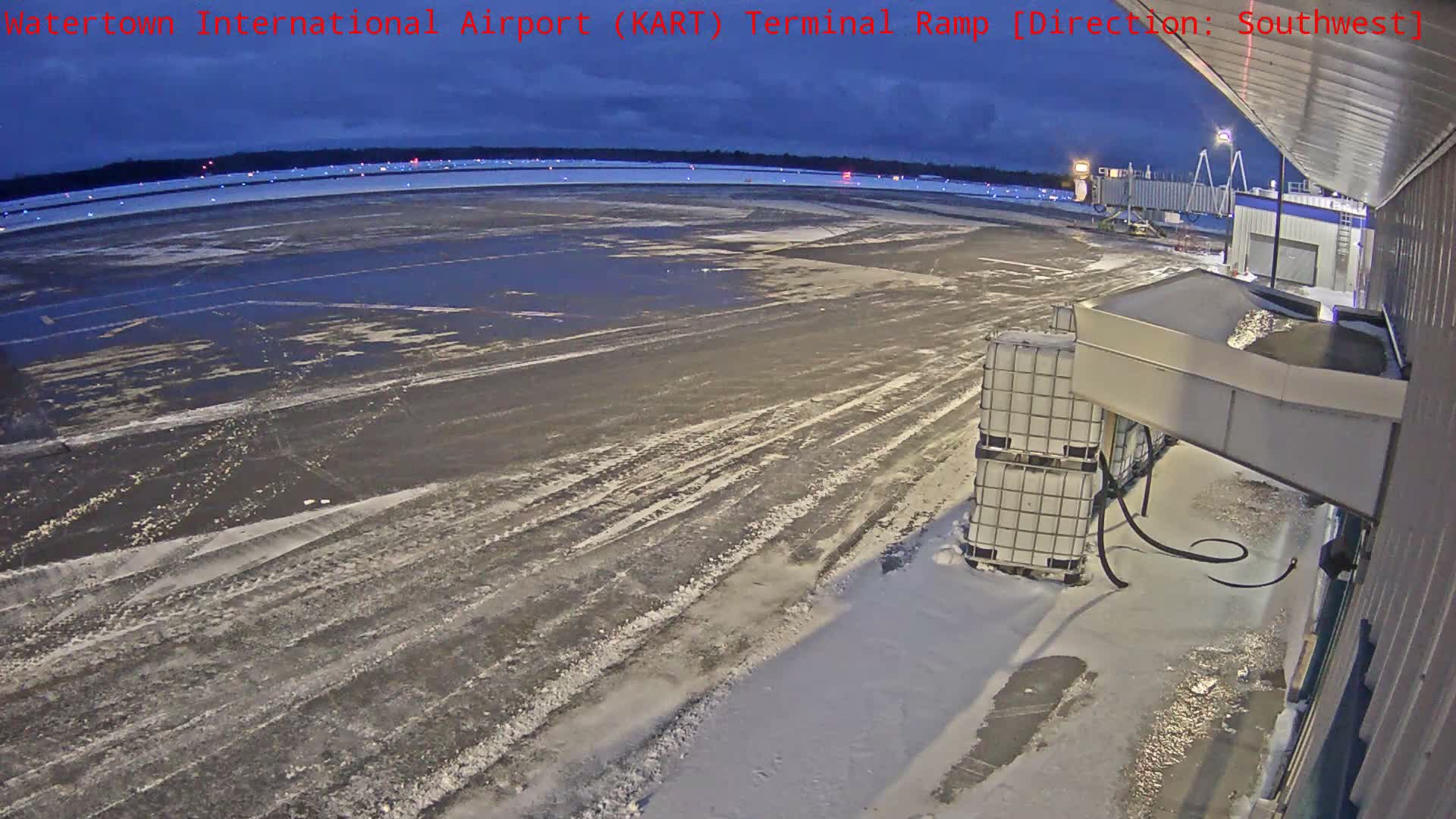 A regional jet is parked at an airport terminal ramp at night, with the ground partially covered in snow and ice under clear skies.