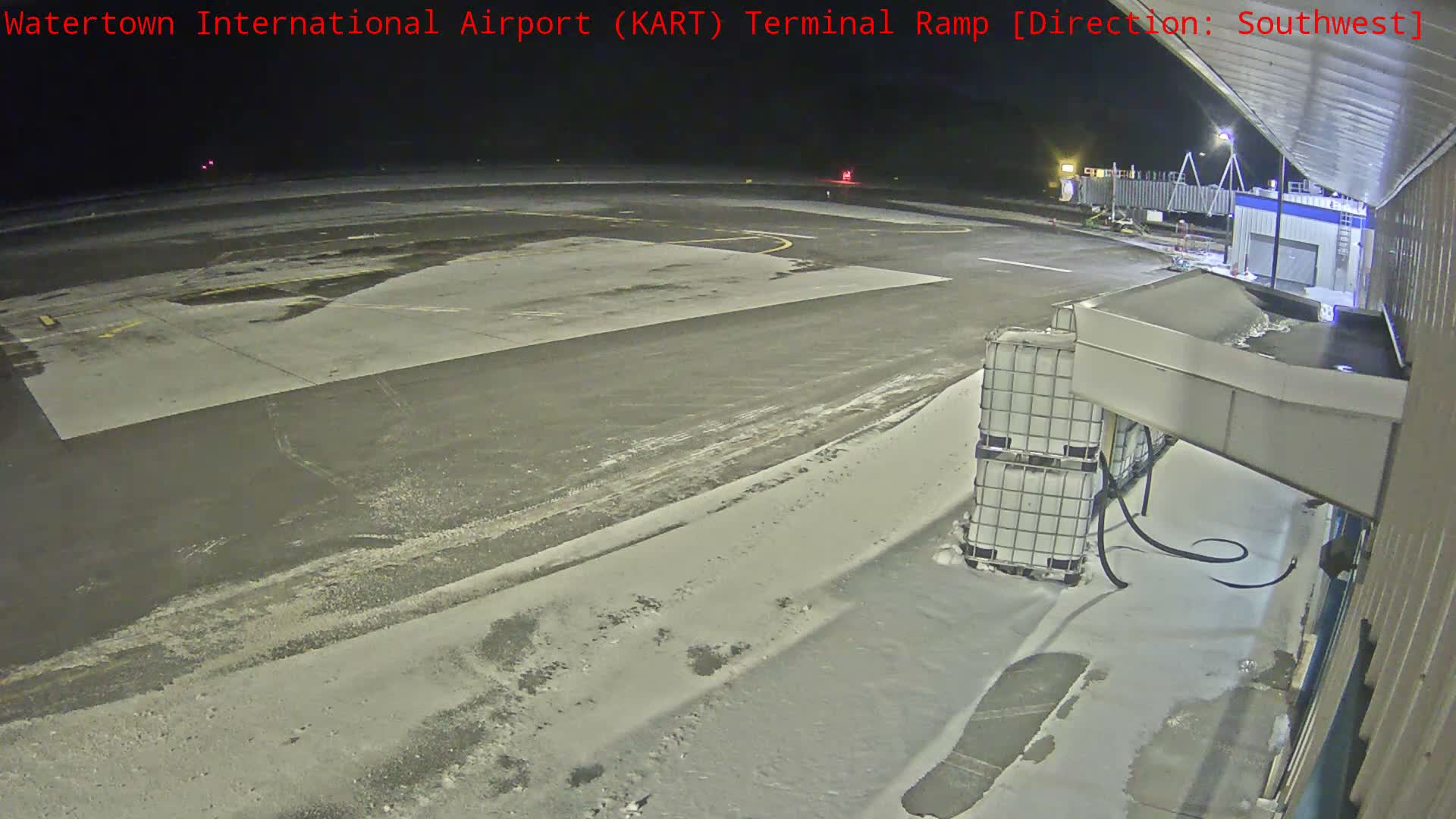 A regional jet is parked at an airport terminal ramp at night, with the ground partially covered in snow and ice under clear skies.