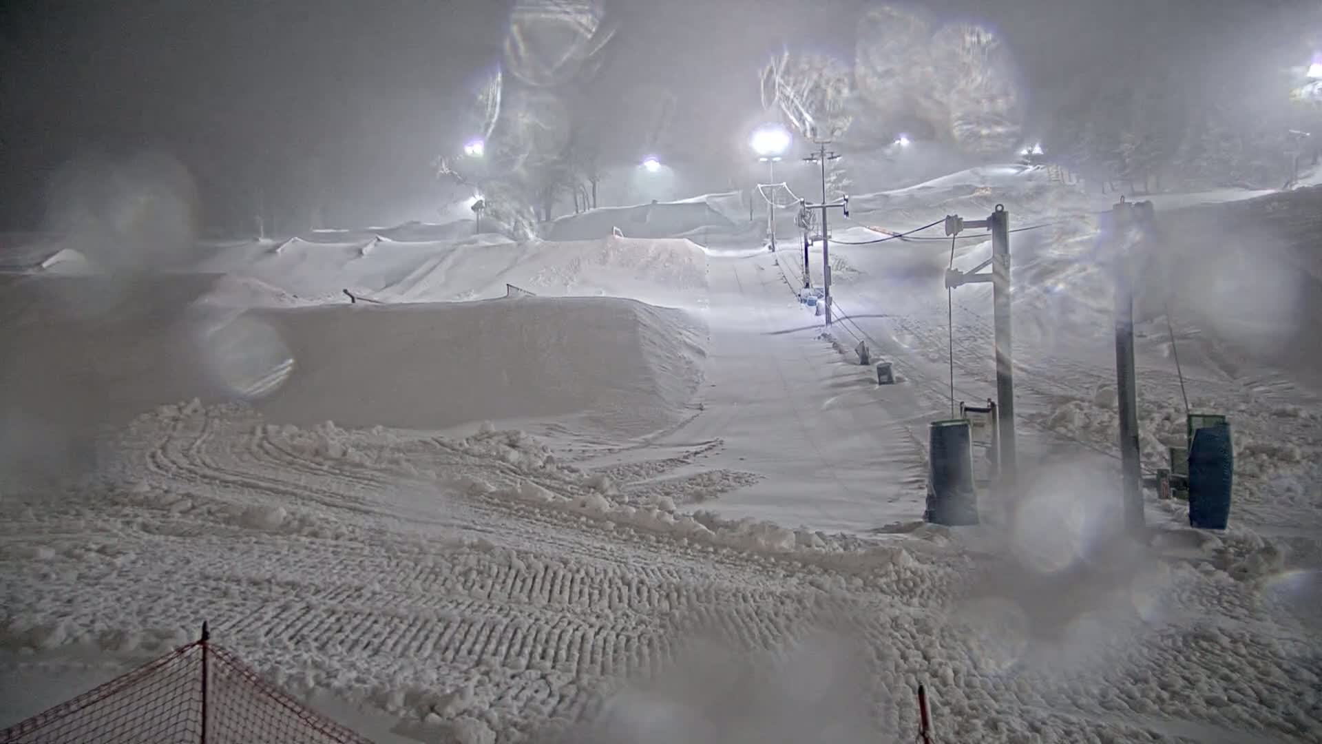 A snow-covered ski slope with a lift and lights is visible during a heavy snowstorm at night.