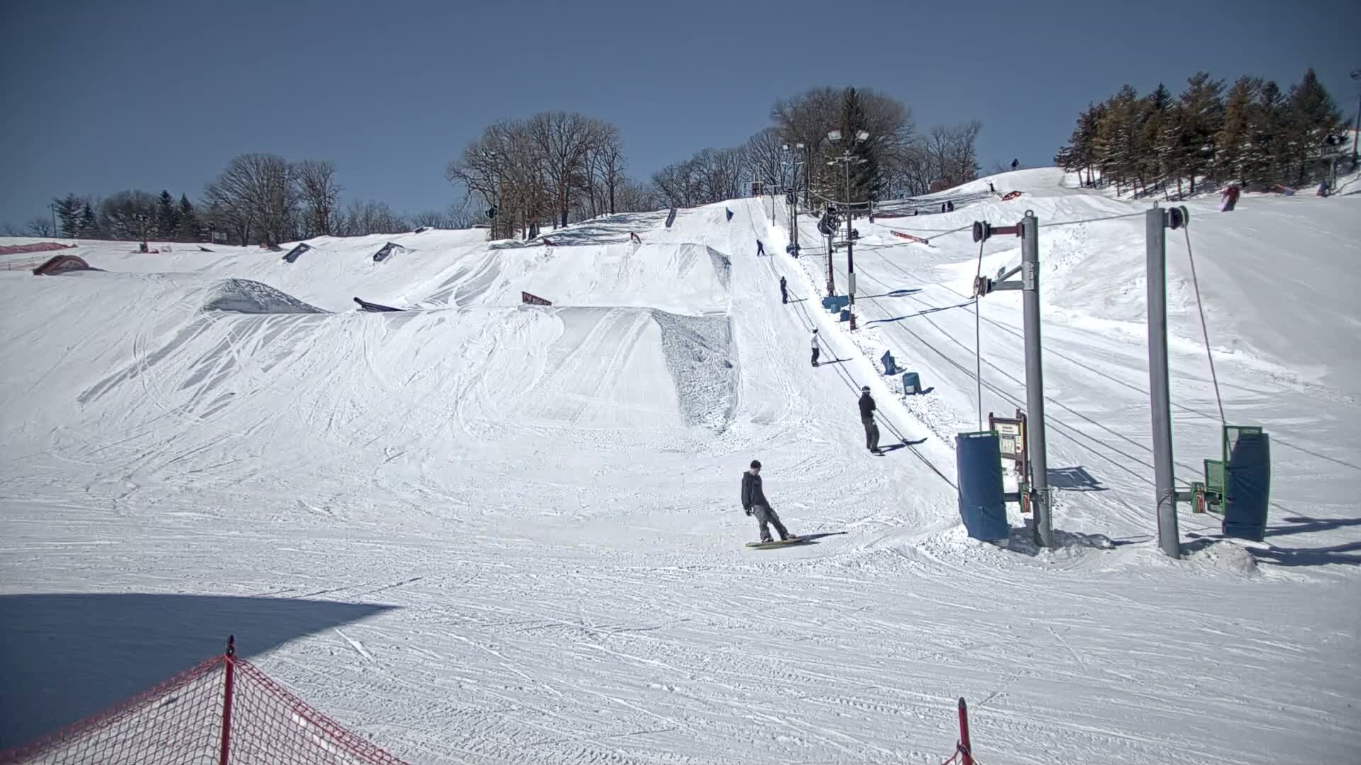 A snow-covered ski slope with several snowboarders and skiers using a chairlift on a sunny day.