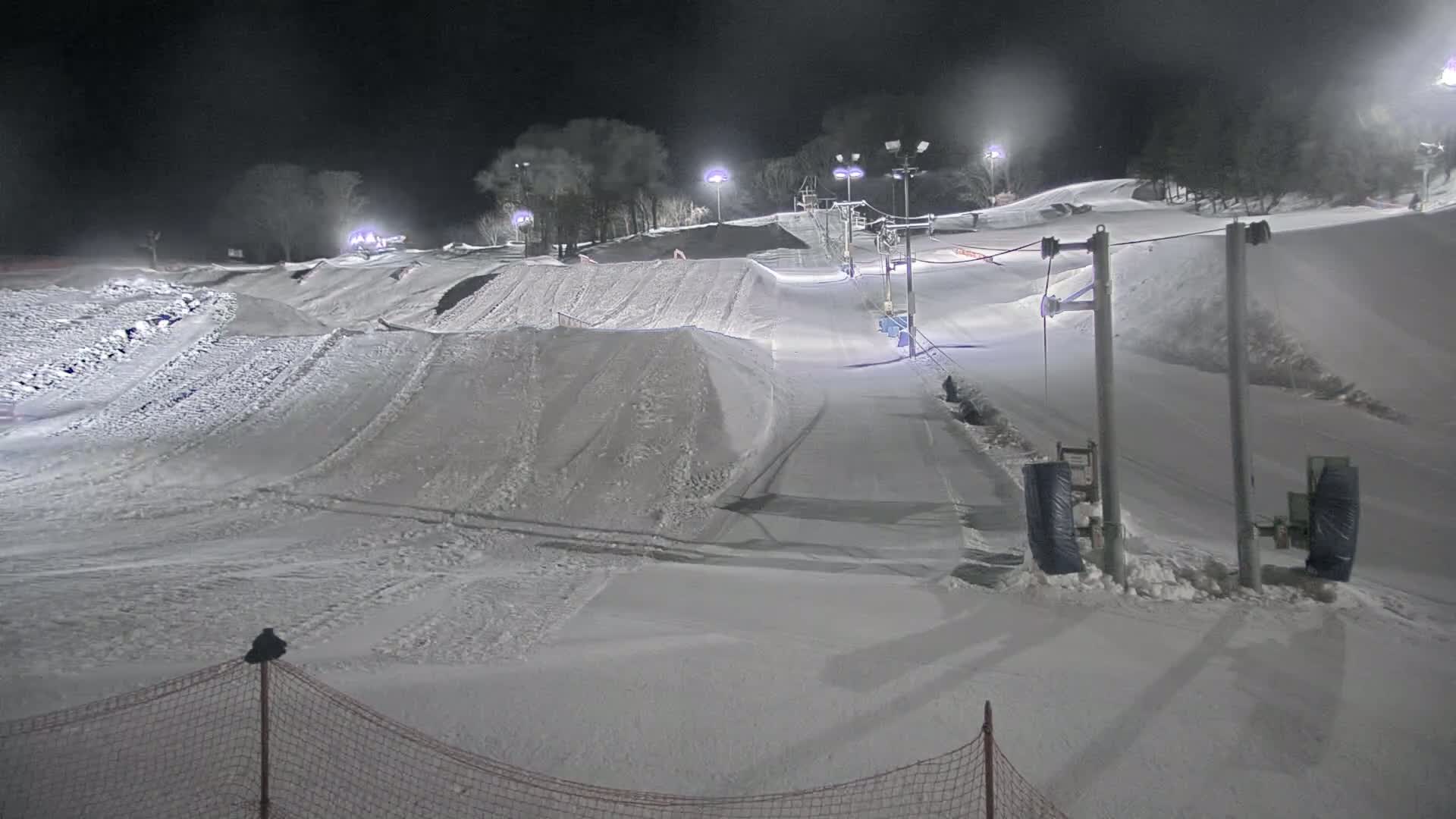 A snow-covered tubing hill is illuminated at night, with a ski lift and several runs visible.