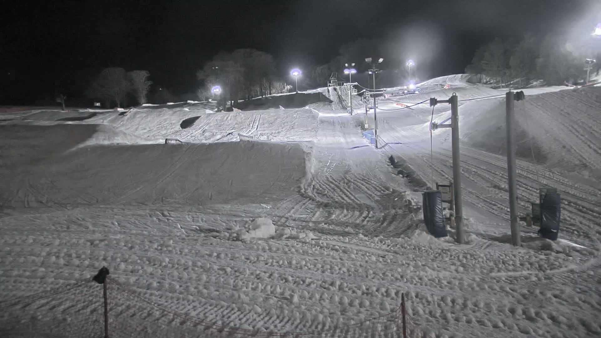 A snow-covered ski slope is illuminated at night by artificial lights.