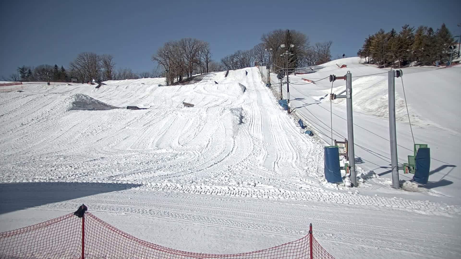 A snow-covered ski slope with a tow rope lift is visible under a clear, sunny sky.