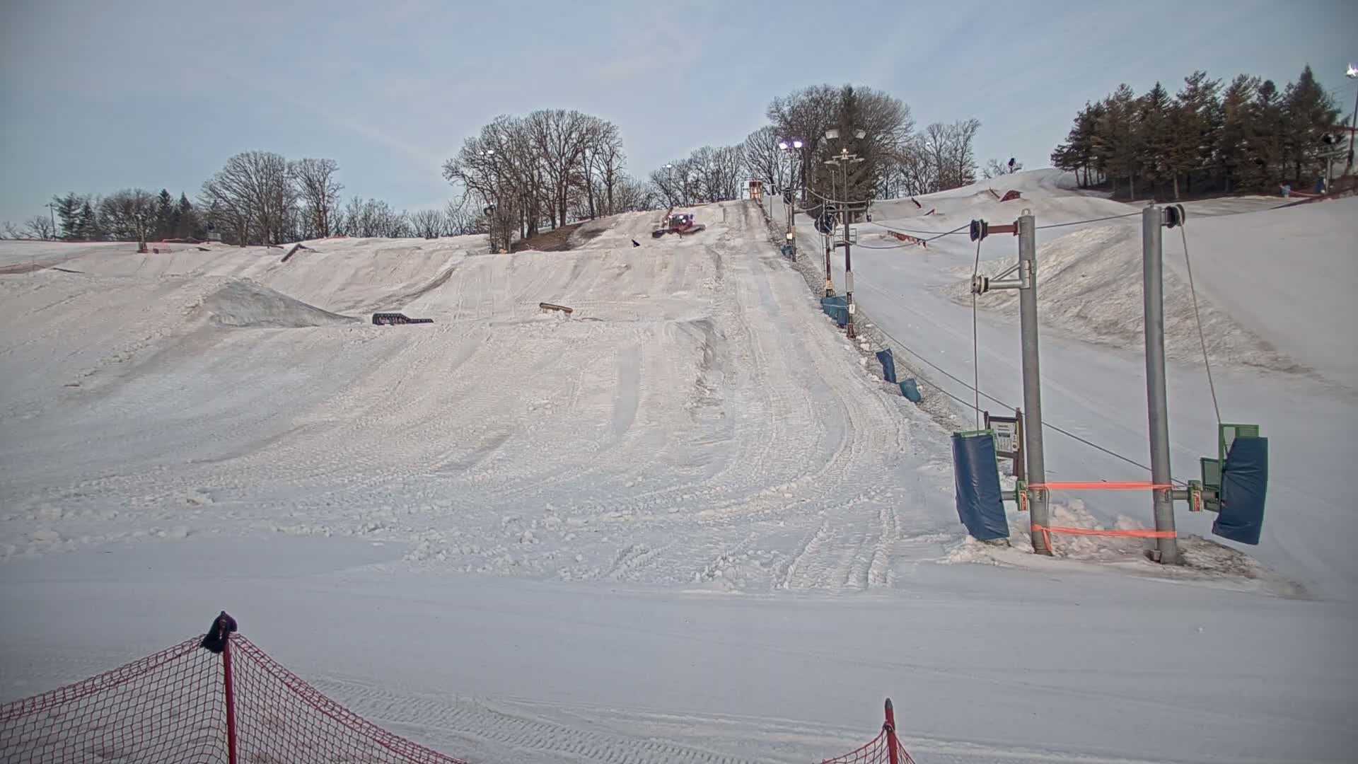 A snow-covered ski slope with a tow rope lift, under a cloudy sky.
