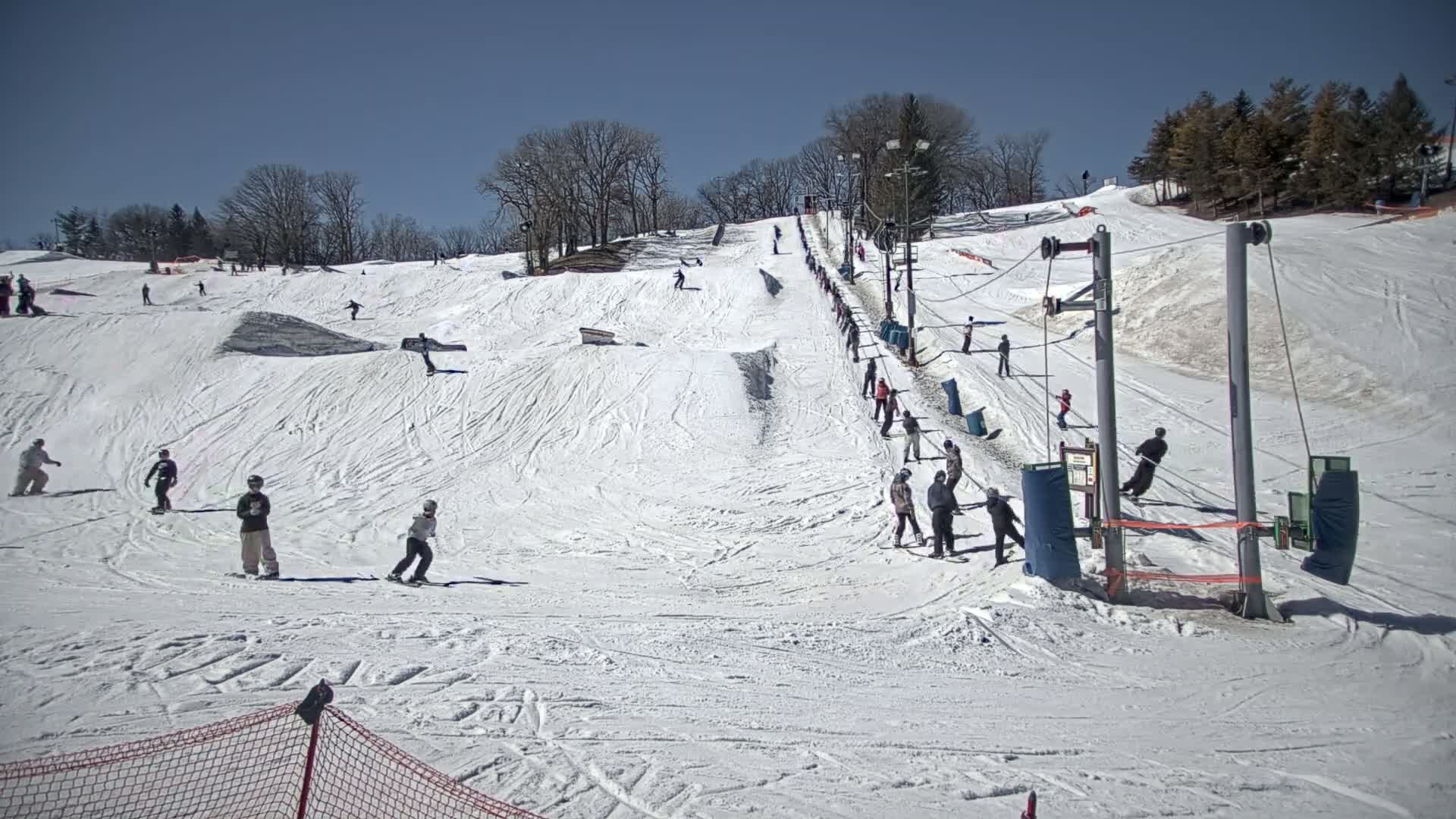 A ski slope with several skiers and snowboarders on a sunny day.