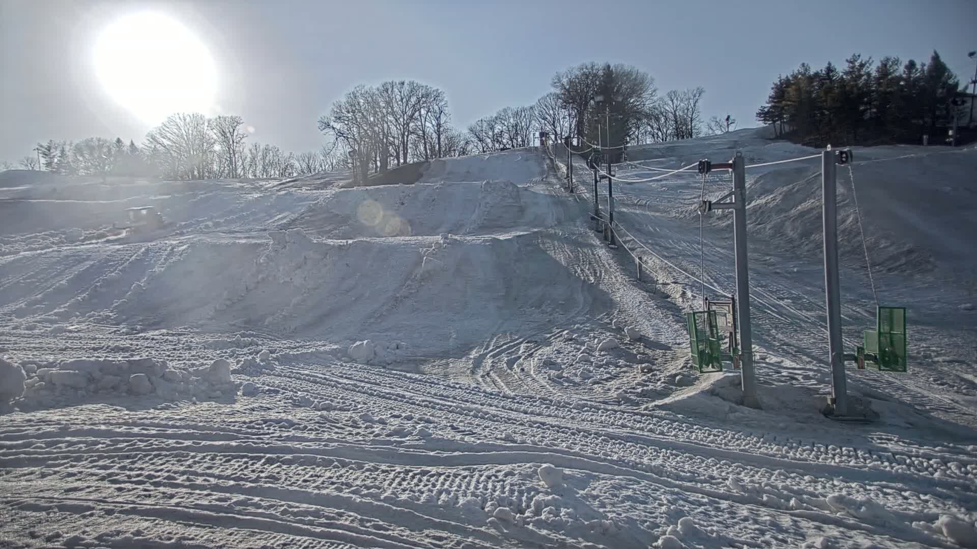 A snow-covered ski slope with a chairlift under a bright, sunny sky.