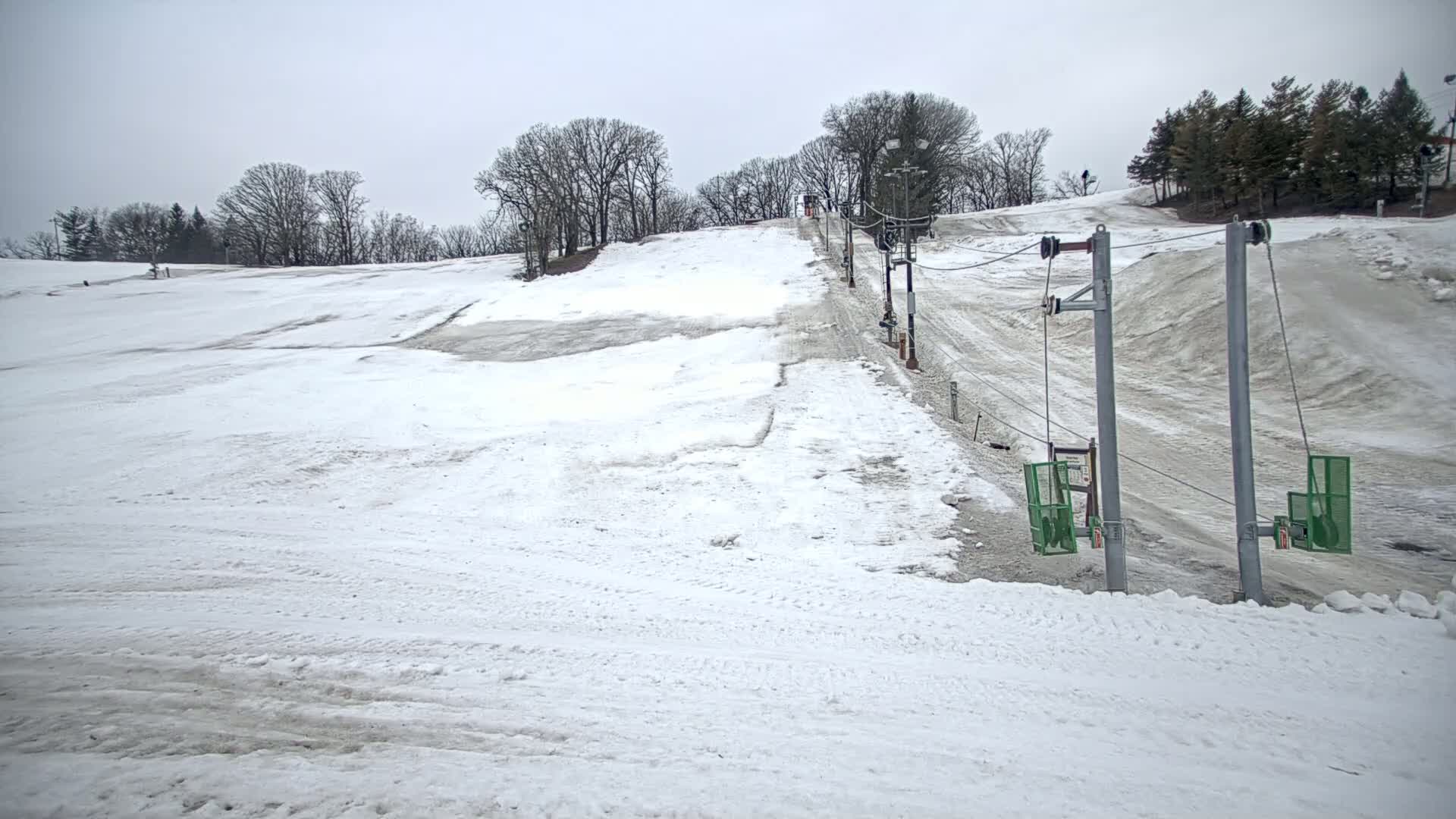 A snow-covered ski slope with a sparsely used surface lift on an overcast day.